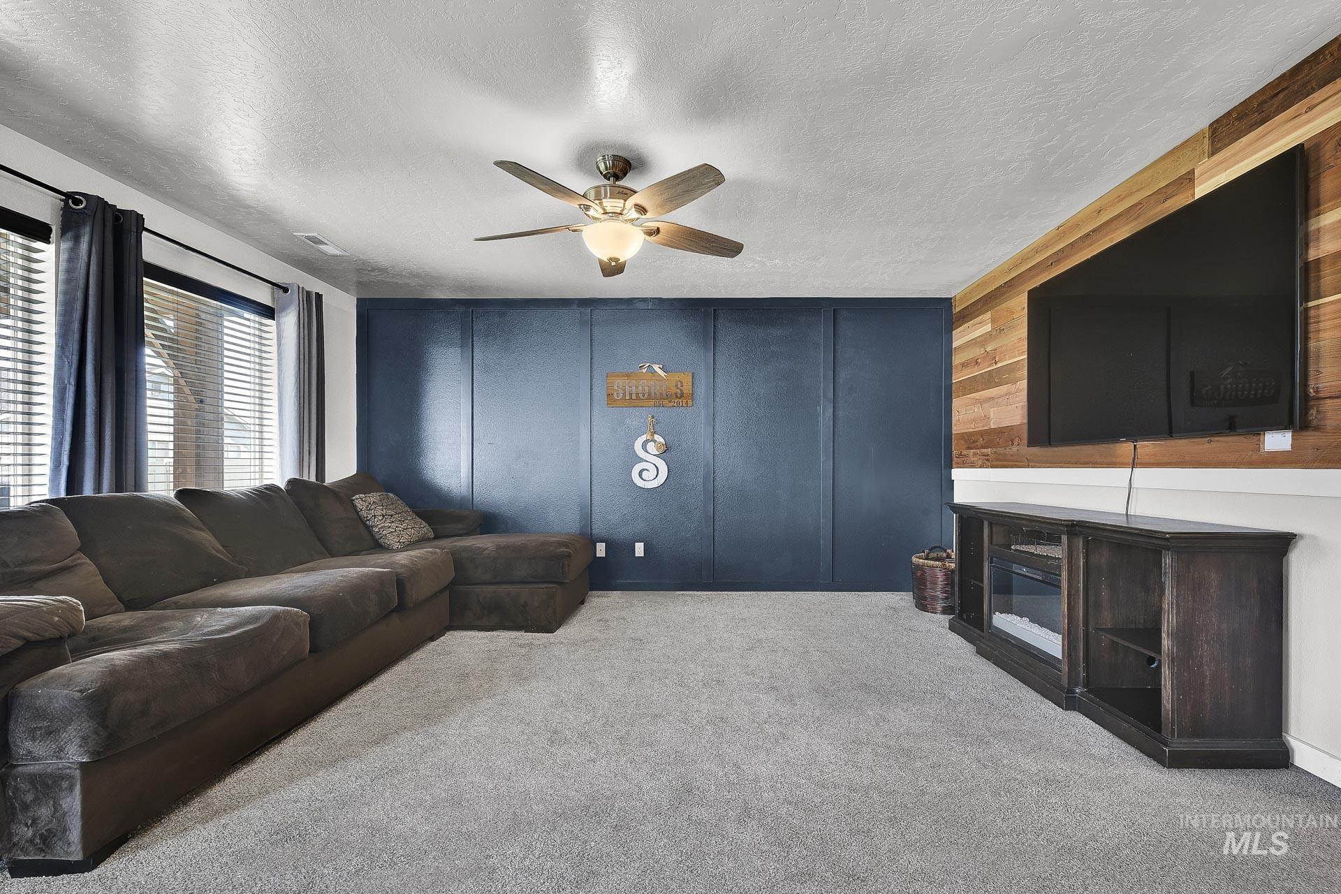 Living room featuring a textured ceiling, carpet floors, a decorative wall, and ceiling fan