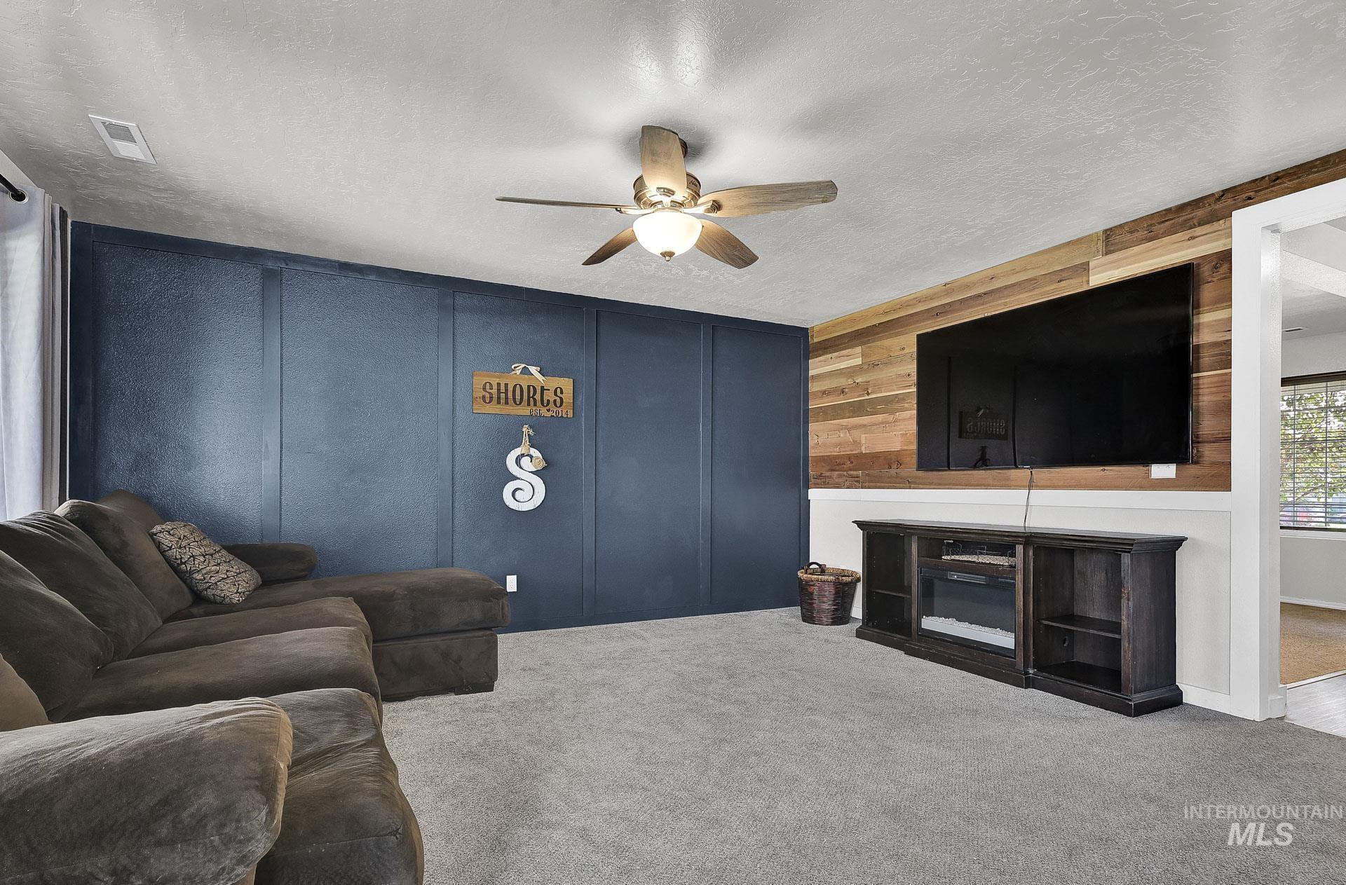 Carpeted living room with a textured ceiling, a decorative wall, a ceiling fan, and wood walls