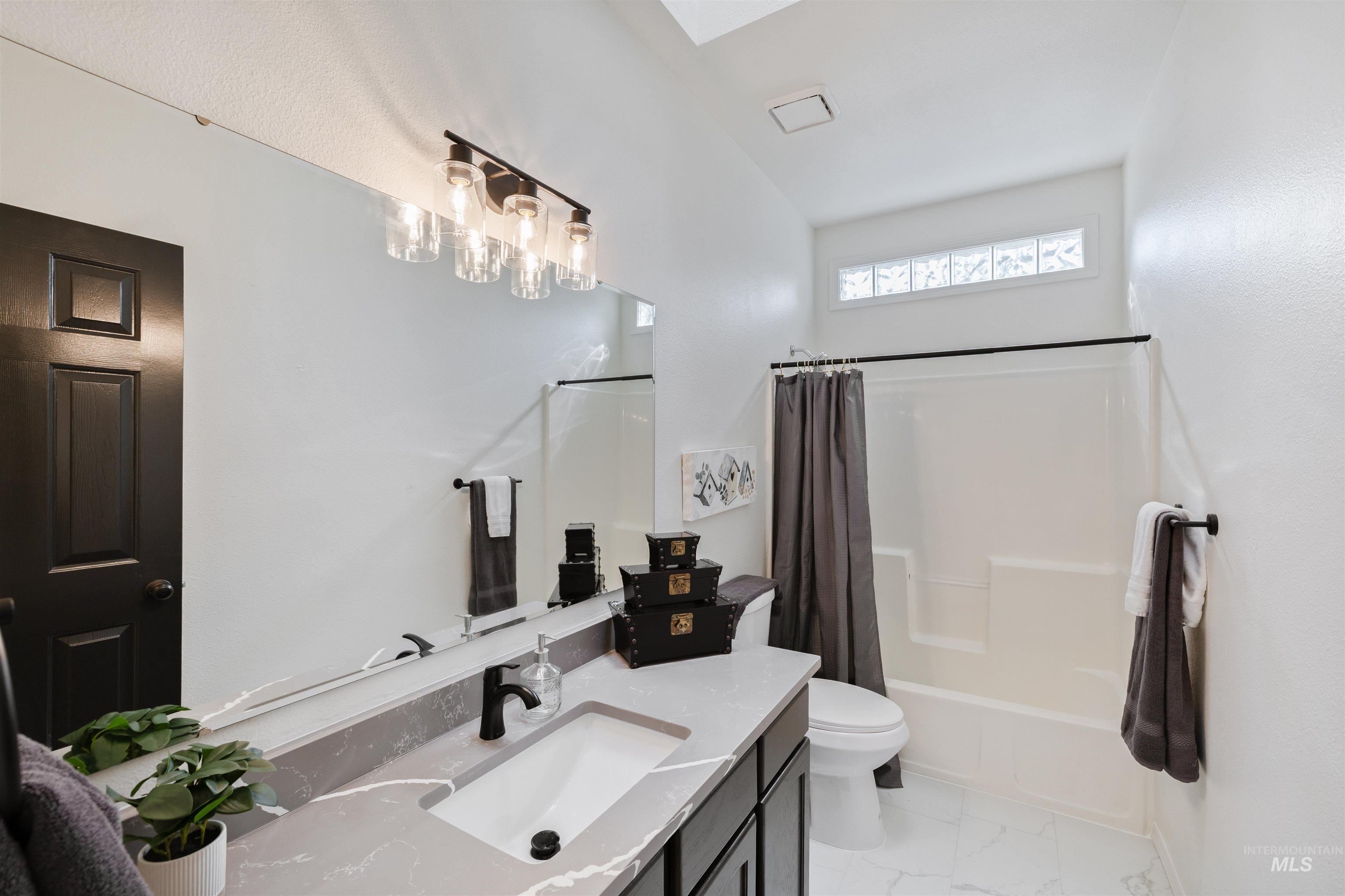 Bathroom featuring shower / bath combination with curtain, vanity, and light marble finish flooring