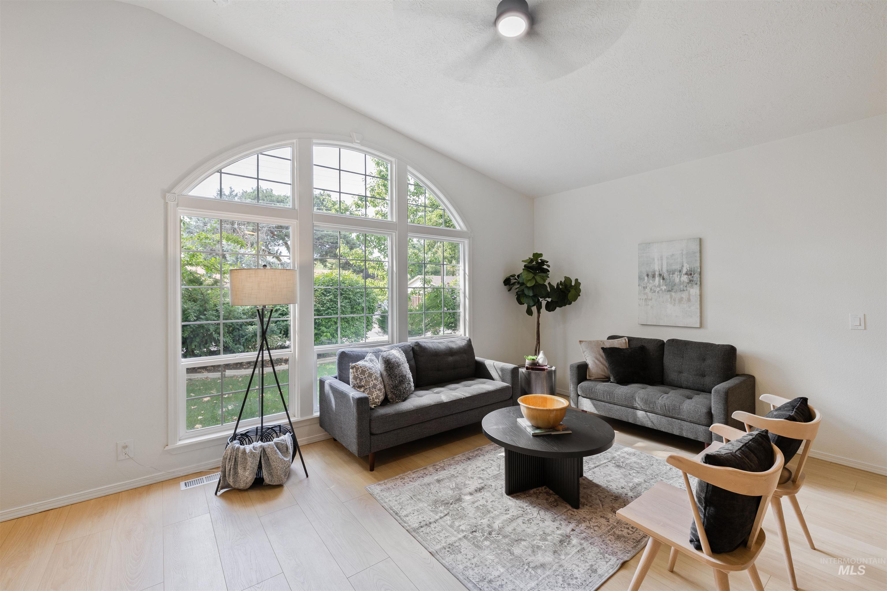 Living area featuring light wood-style floors, vaulted ceiling, and a ceiling fan