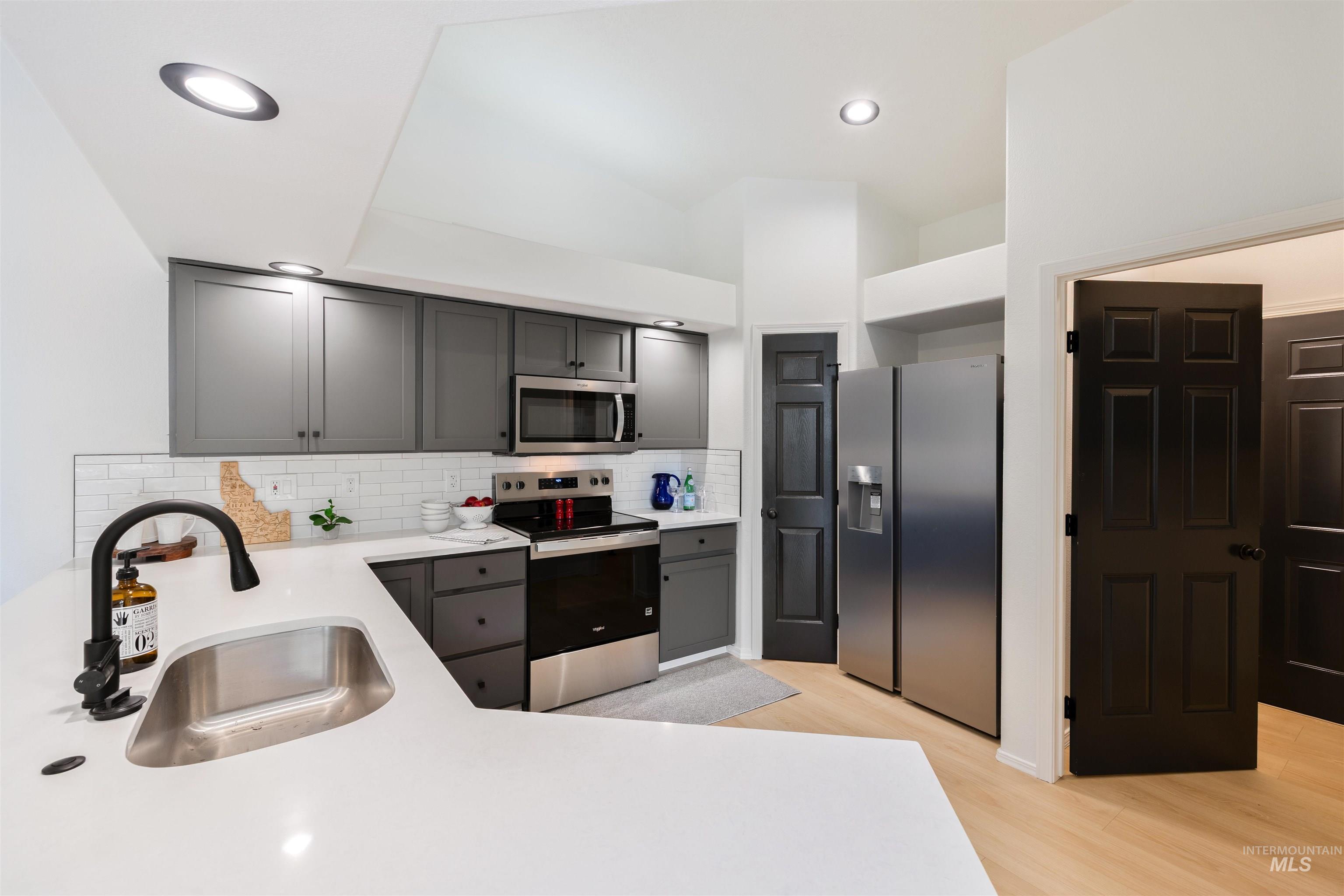 Kitchen featuring appliances with stainless steel finishes, decorative backsplash, gray cabinets, light wood-type flooring, and light stone countertops