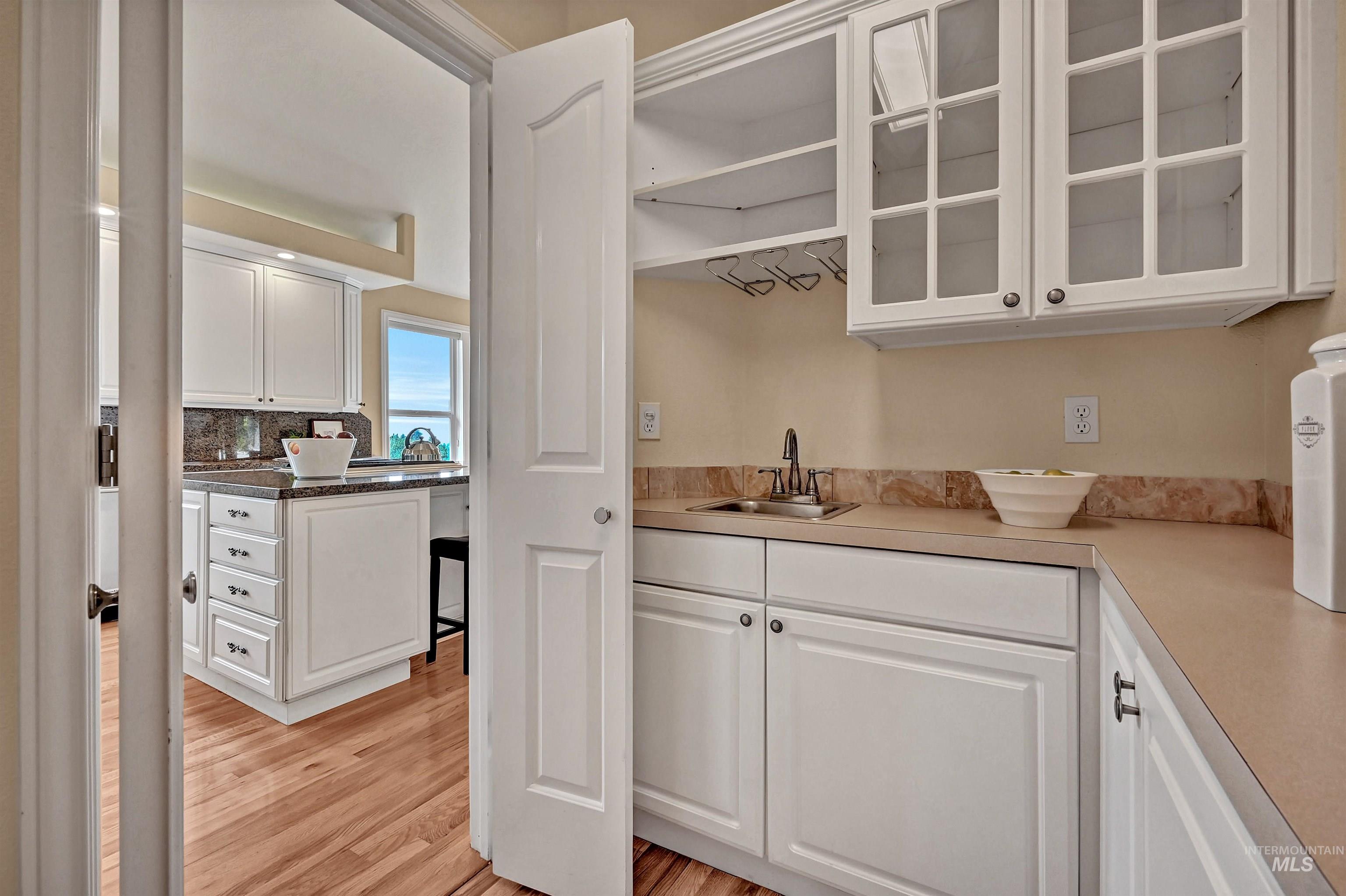 Pantry with white cabinetry, light wood finished floors, glass insert cabinets, and light countertops