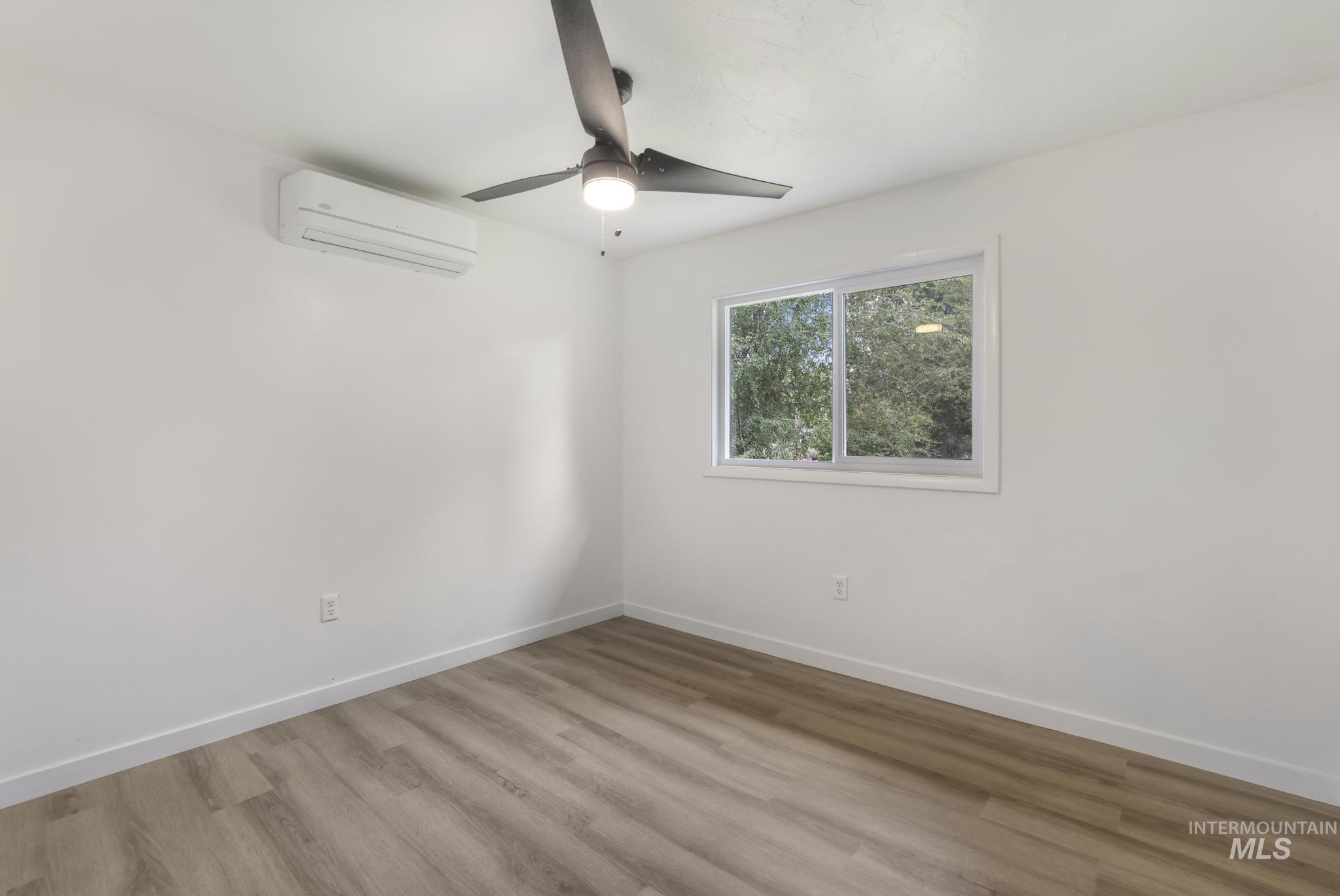 Empty room featuring wood finished floors, an AC wall unit, and a ceiling fan