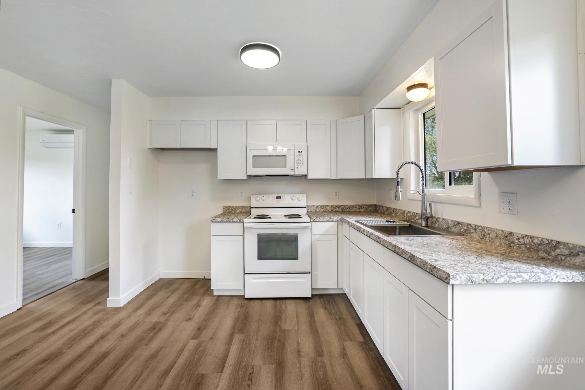Kitchen featuring white appliances, white cabinets, light countertops, and dark wood-style flooring