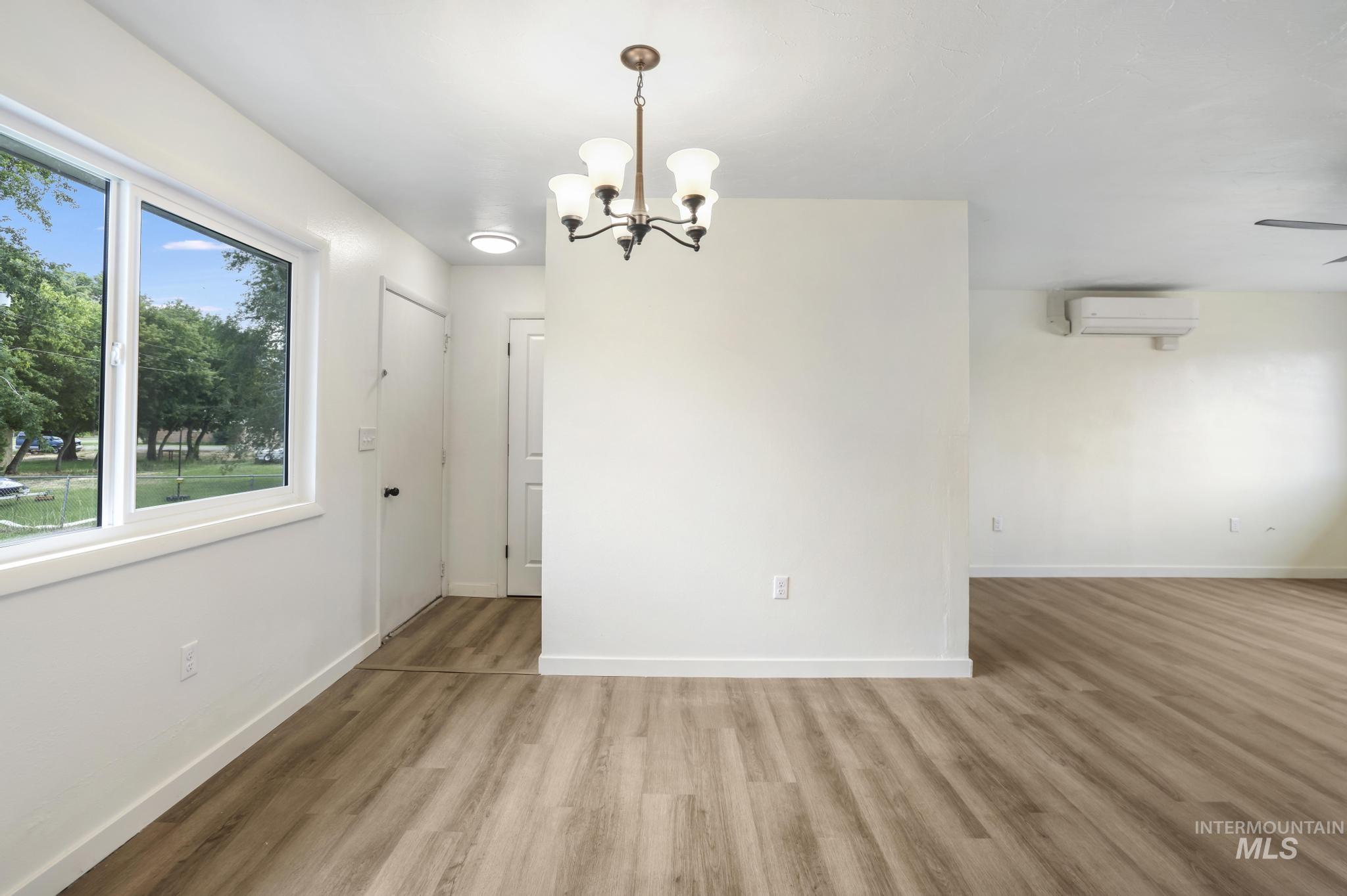 Unfurnished dining area featuring light wood-style flooring, a chandelier, and a wall unit AC