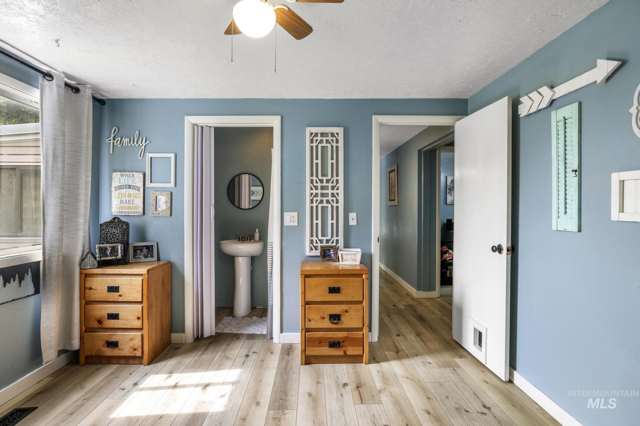Bedroom featuring a textured ceiling, light wood-style flooring, ensuite bath, and ceiling fan