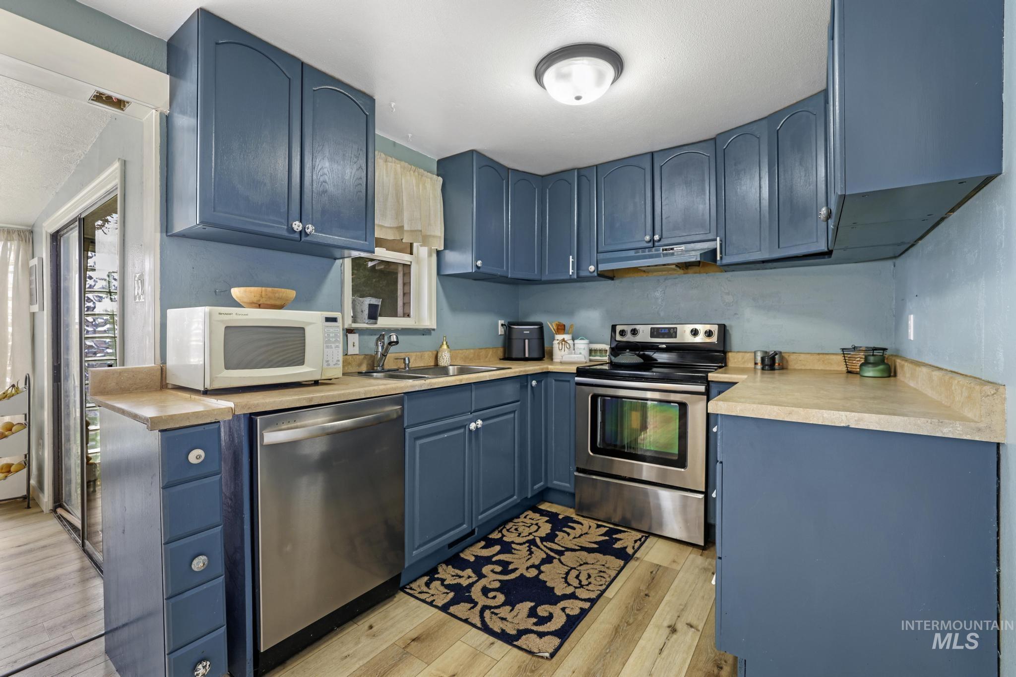Kitchen with blue cabinets, light countertops, stainless steel appliances, light wood-style flooring, and under cabinet range hood