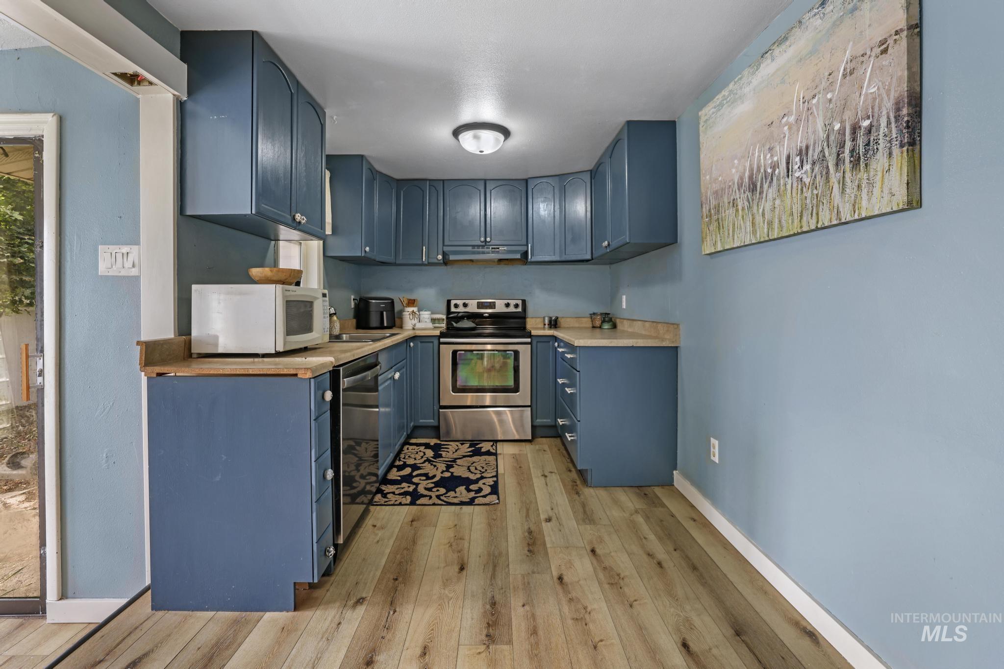 Kitchen featuring blue cabinetry, stainless steel appliances, light wood finished floors, and butcher block countertops