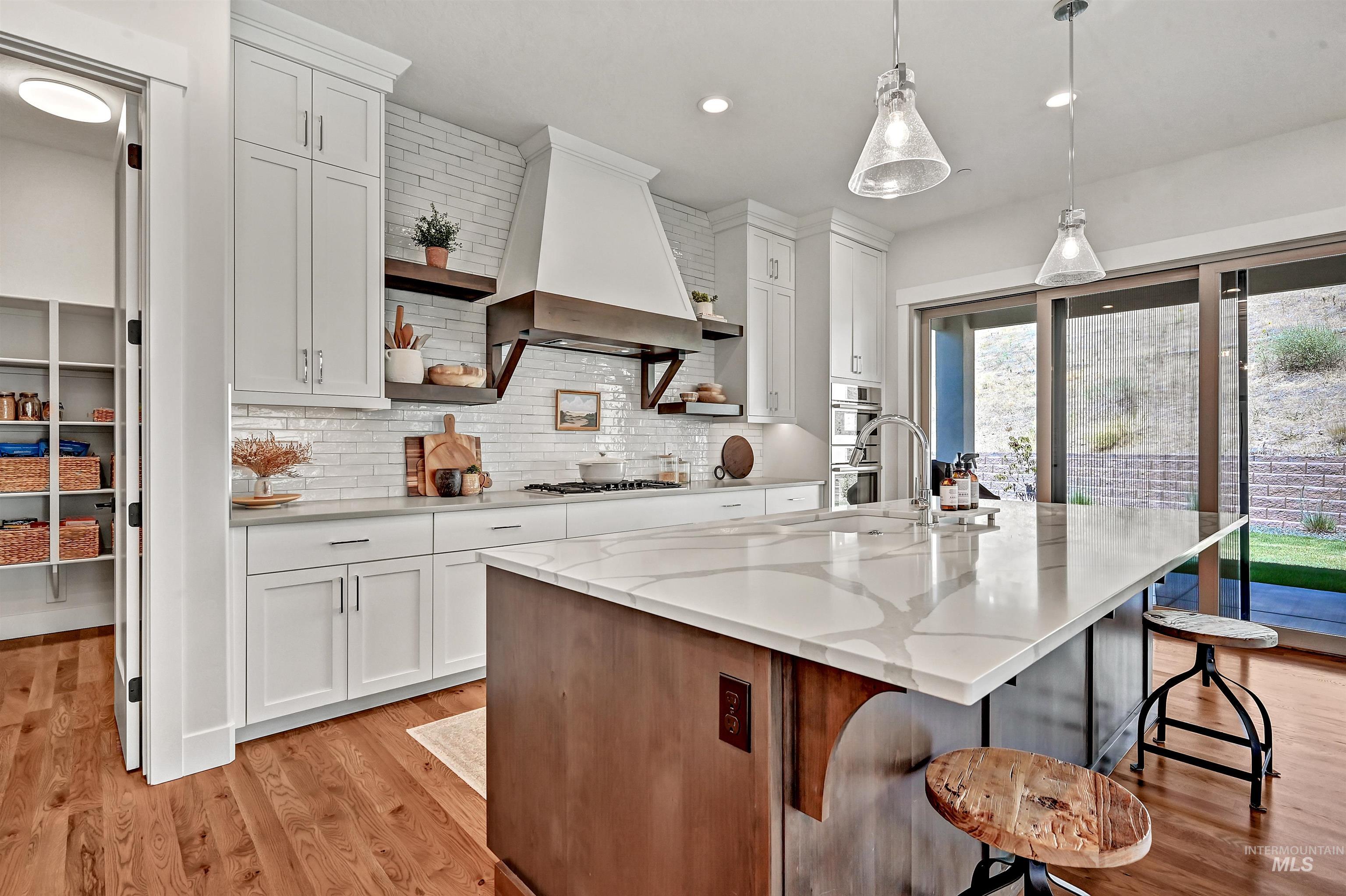 Kitchen with open shelves, a breakfast bar area, an island with sink, light wood-style flooring, and light stone counters