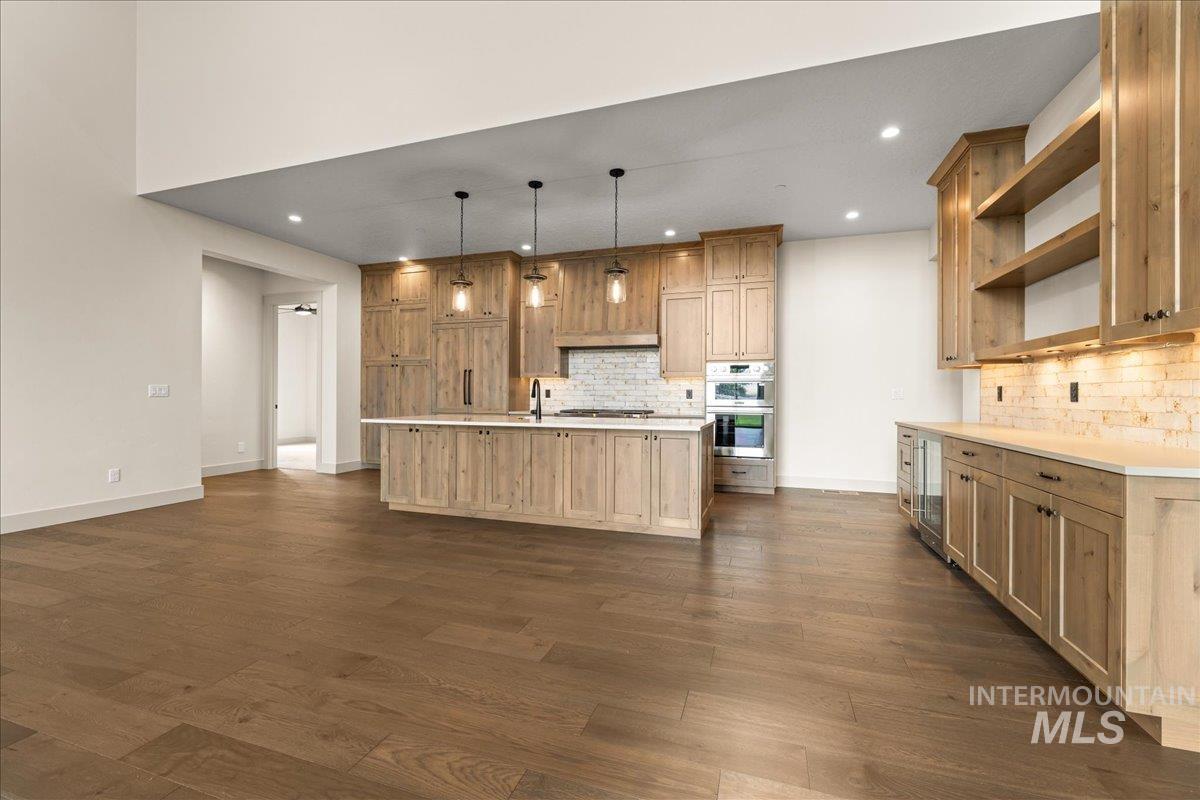 Kitchen featuring open shelves, pendant lighting, a center island with sink, recessed lighting, and dark wood-type flooring