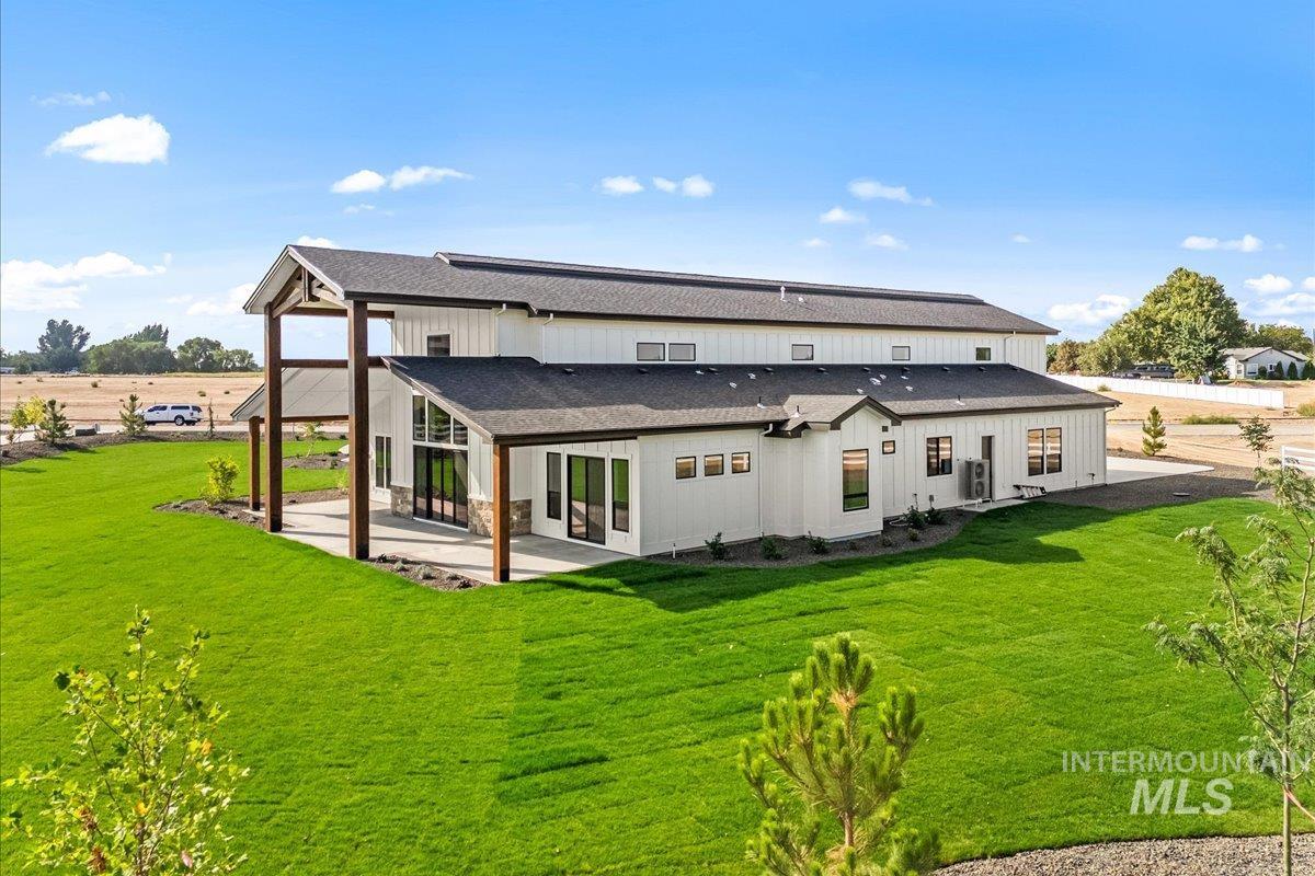 Back of property featuring a patio area, a shingled roof, a lawn, and board and batten siding