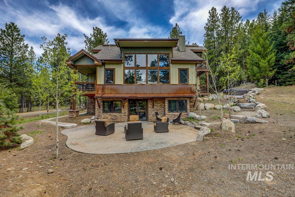 Rear view of house with a patio, stone siding, a chimney, a balcony, and roof with shingles