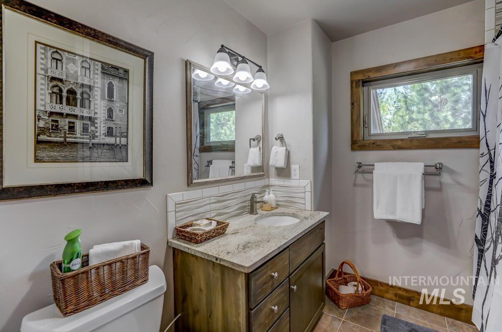 Half bathroom with plenty of natural light, vanity, light tile patterned floors, and decorative backsplash