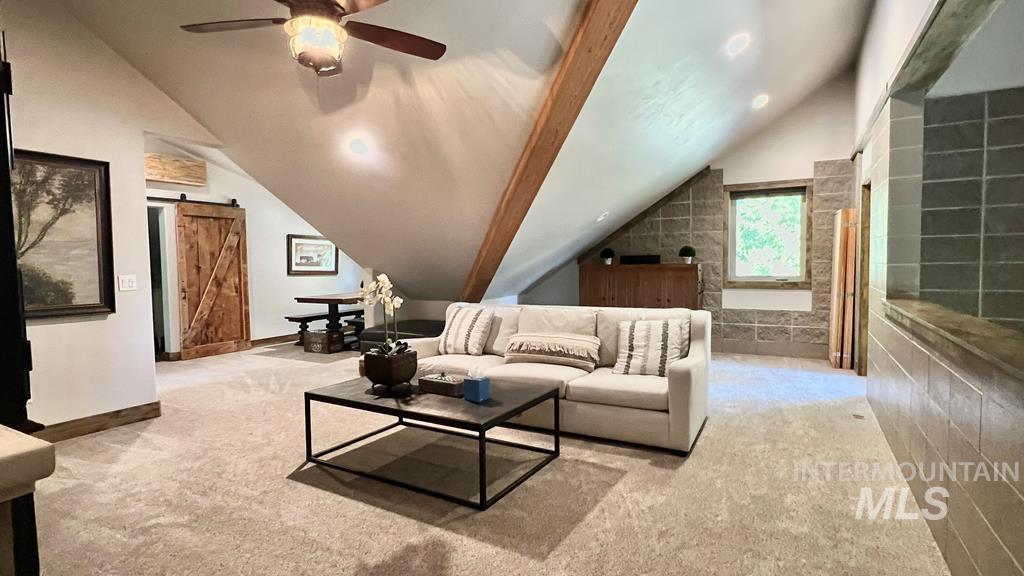 Living room featuring a barn door, lofted ceiling, light colored carpet, and ceiling fan