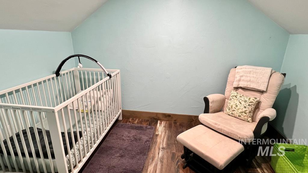 Bedroom featuring dark wood finished floors, a nursery area, and lofted ceiling