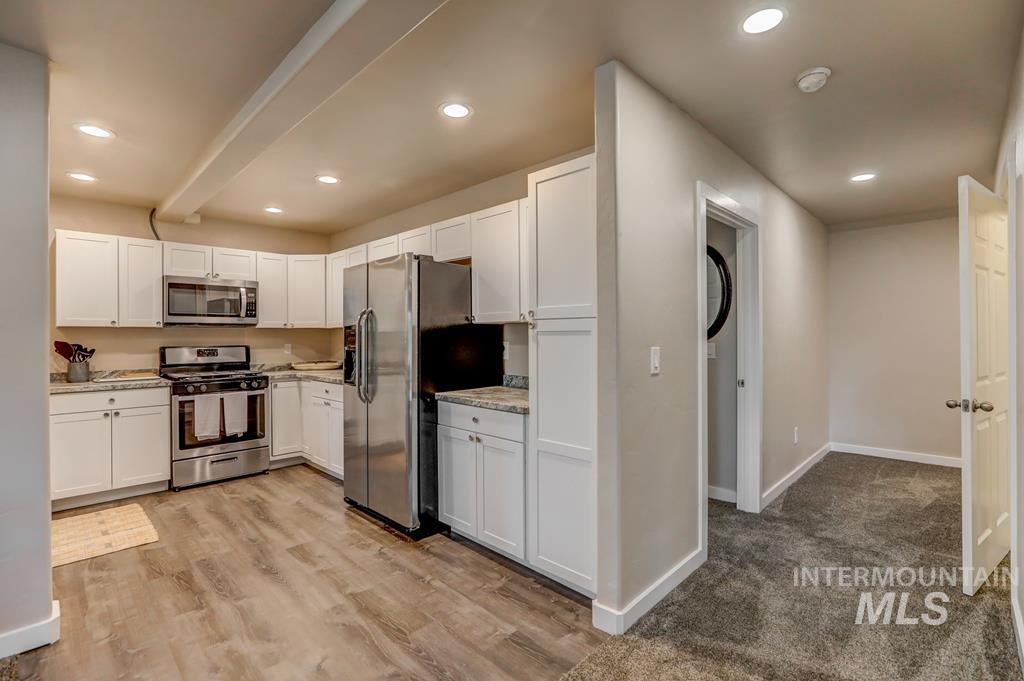 Kitchen featuring stainless steel appliances, white cabinets, recessed lighting, light wood-style flooring, and light stone countertops