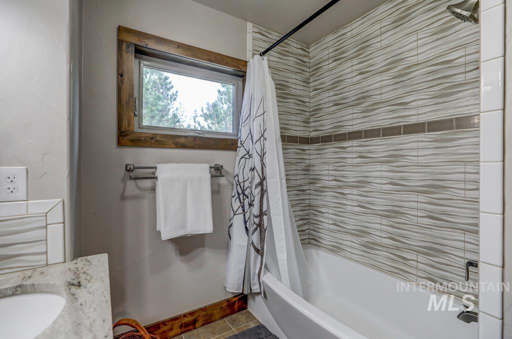 Bathroom featuring shower / tub combo, vanity, and dark tile patterned flooring