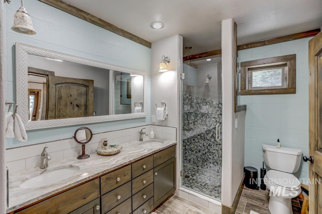 Full bath featuring a stall shower, double vanity, and tile walls