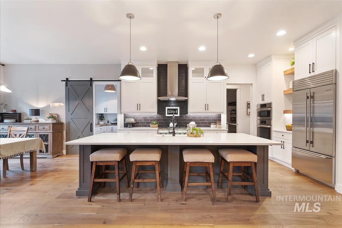 Kitchen with a barn door, white cabinets, decorative backsplash, appliances with stainless steel finishes, and a kitchen breakfast bar