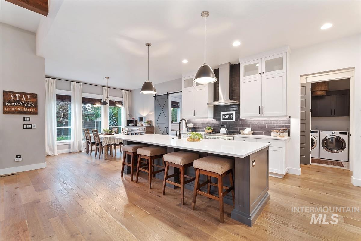 Kitchen featuring a barn door, decorative backsplash, white cabinetry, glass insert cabinets, and hanging light fixtures