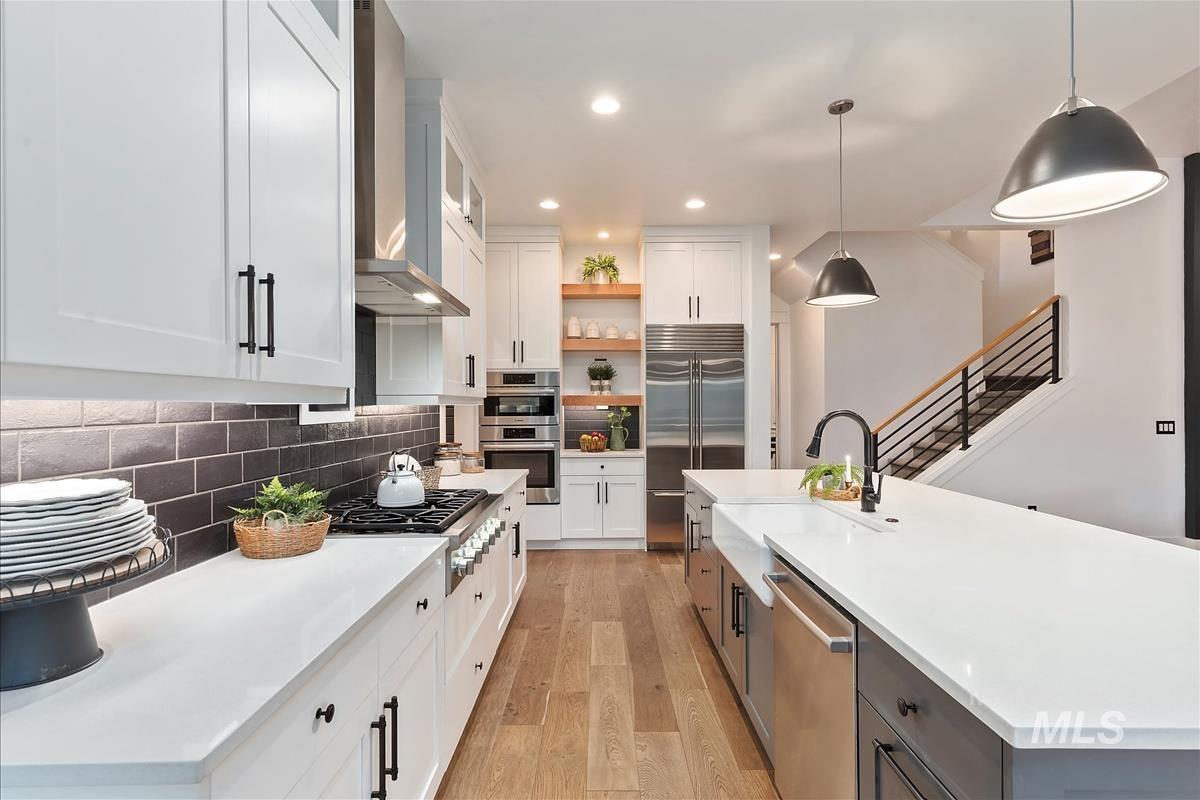 Kitchen with white cabinetry, decorative light fixtures, glass insert cabinets, wall chimney range hood, and a kitchen island with sink