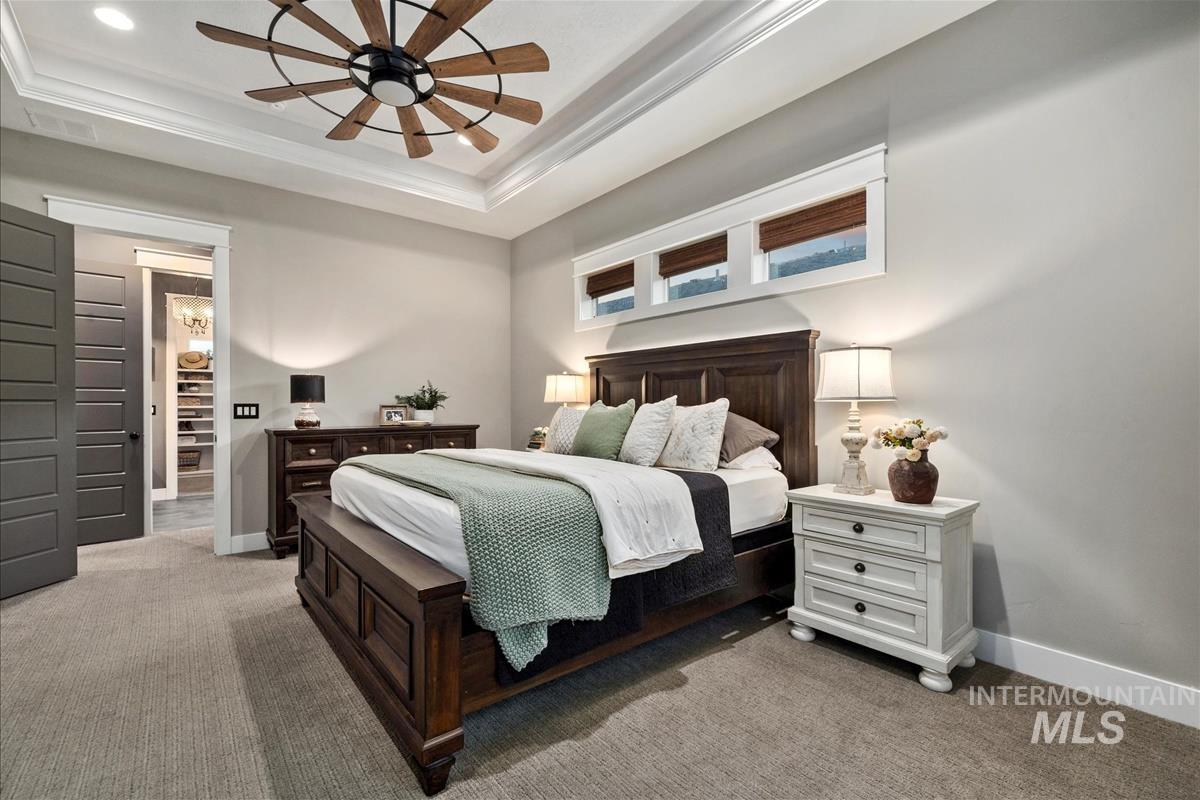 Bedroom with light carpet, a raised ceiling, ornamental molding, and a ceiling fan