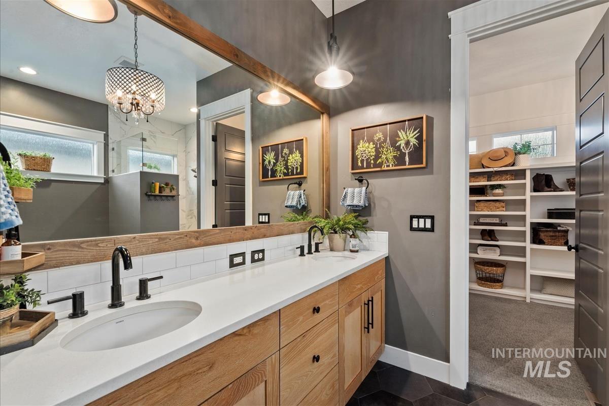 Full bath with plenty of natural light, double vanity, a walk in closet, and dark tile patterned flooring