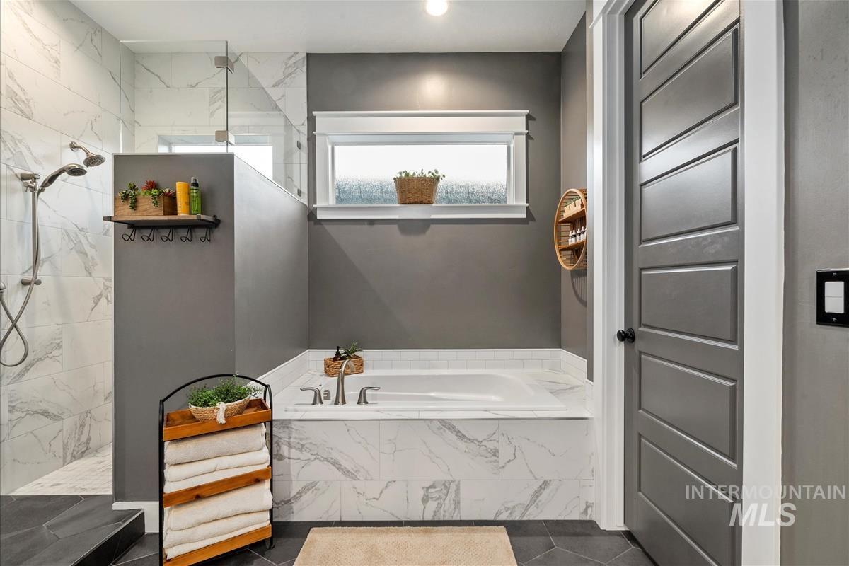Full bath featuring a garden tub, a marble finish shower, and dark tile patterned floors