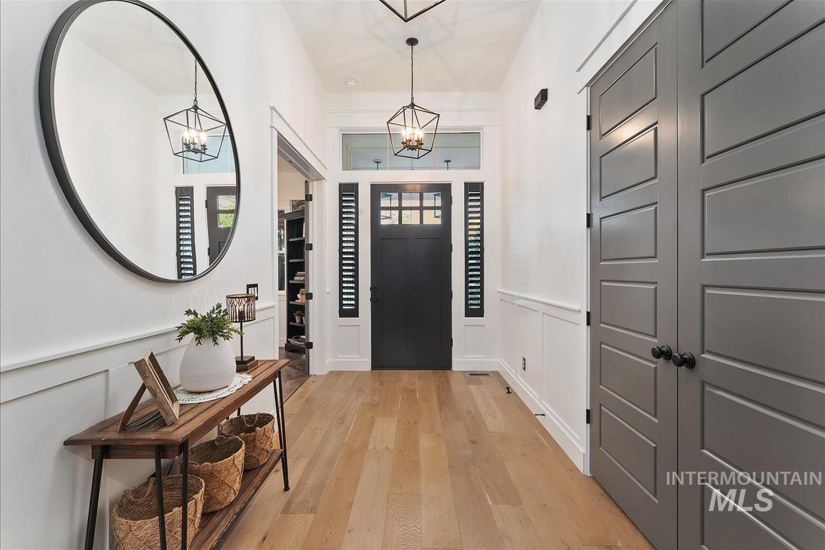 Foyer featuring light wood-style flooring, a decorative wall, a chandelier, and a wainscoted wall