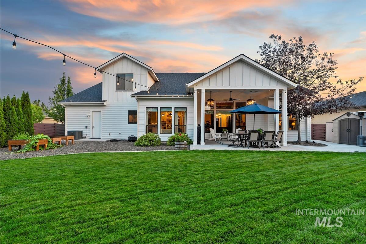 Back of property at dusk featuring board and batten siding, a storage shed, a patio area, and a shingled roof