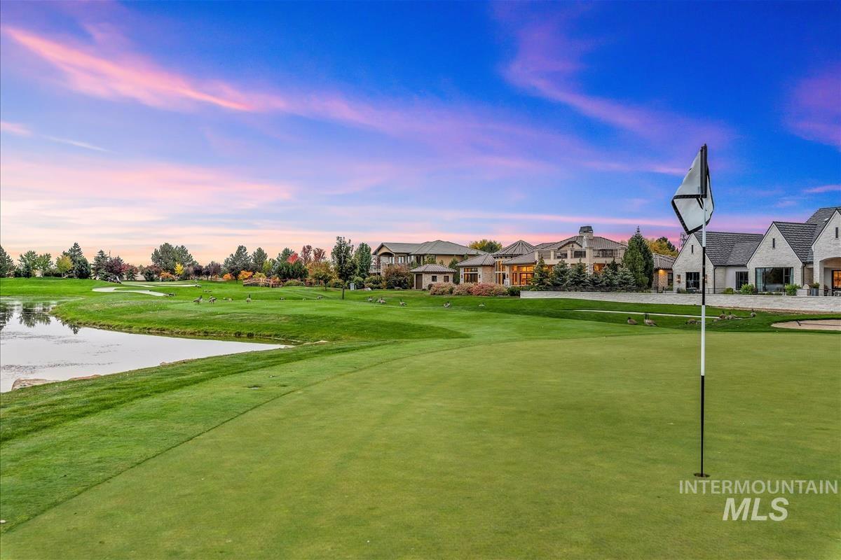 View of community with golf course view, a water view, a yard, and an area to practice putting