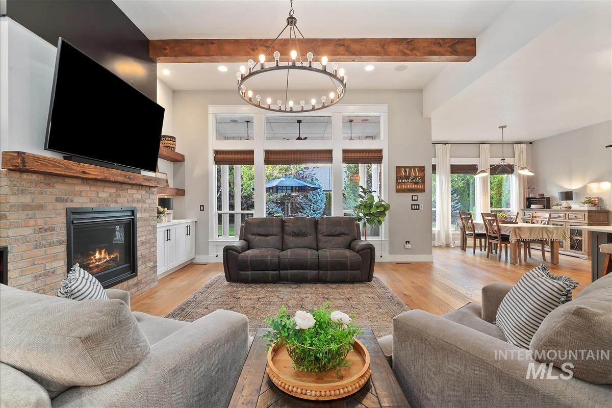 Living room with light wood finished floors, plenty of natural light, beamed ceiling, a brick fireplace, and recessed lighting