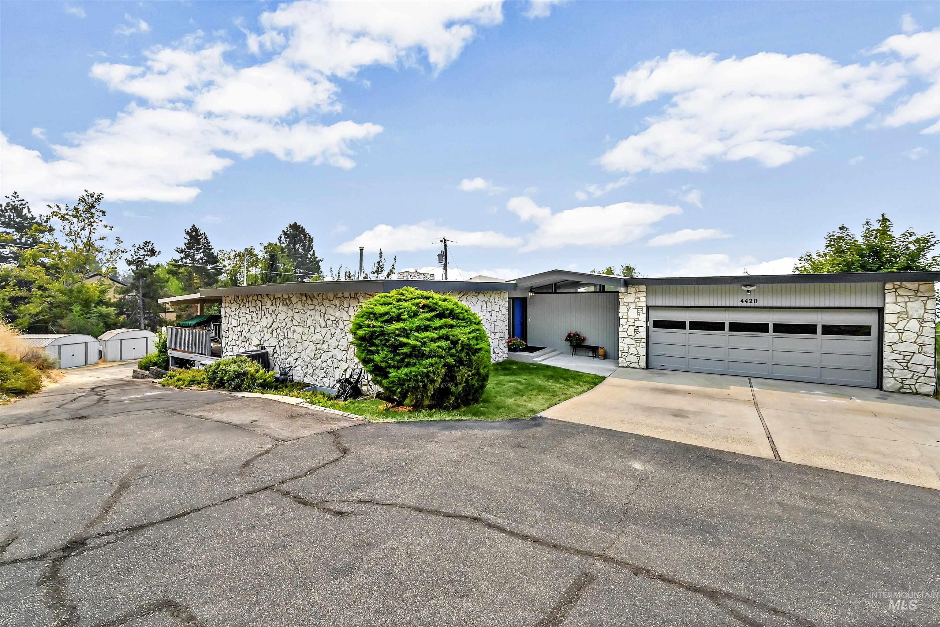 Mid-century modern home with stone siding, driveway, an attached garage, and a storage unit