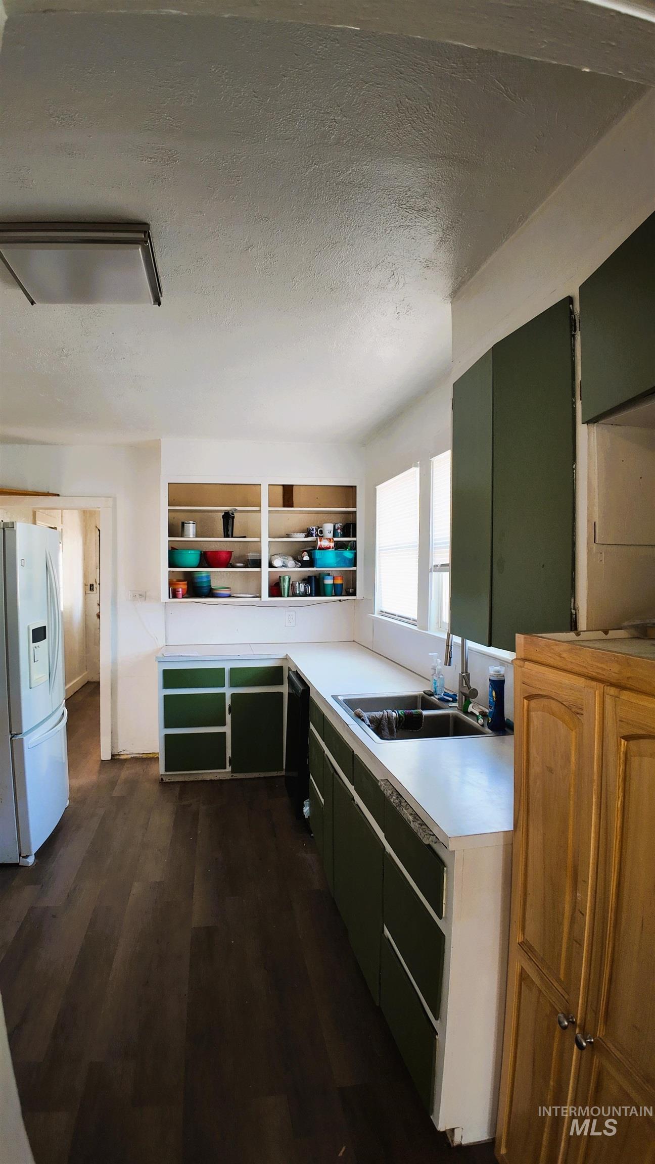 Kitchen with a textured ceiling, dark wood-style floors, light countertops, and white fridge with ice dispenser