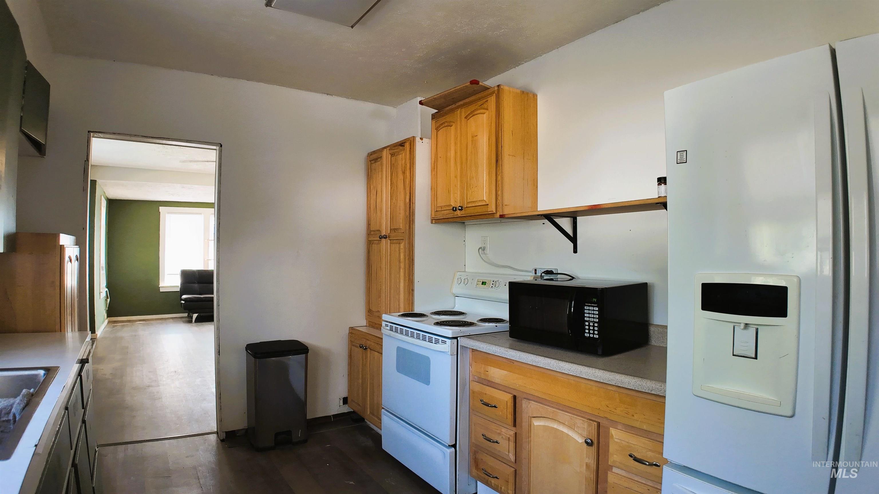 Kitchen featuring white appliances, light countertops, dark wood-style flooring, and brown cabinets