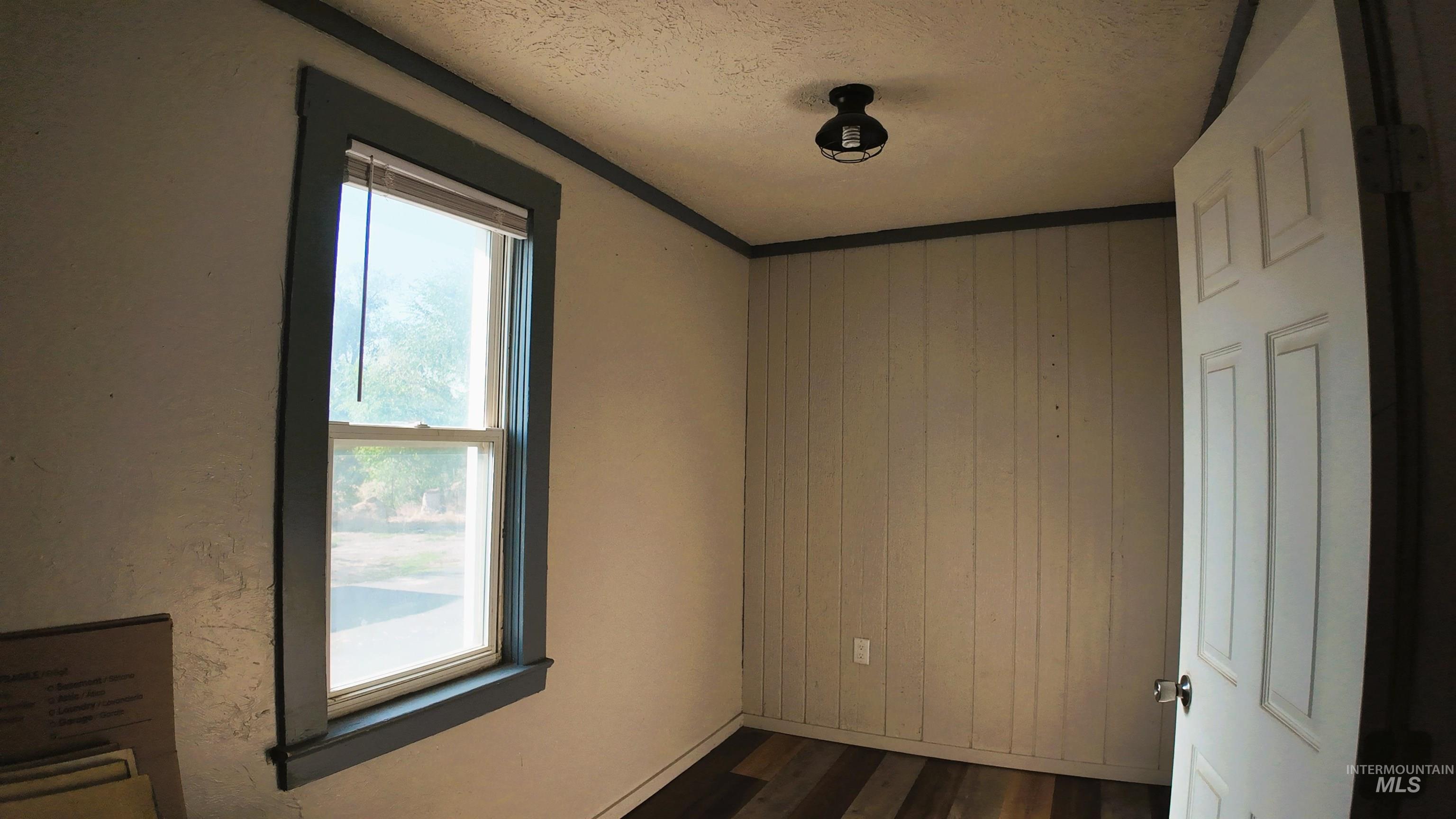 Spare room with dark wood finished floors, wood walls, a textured ceiling, and ornamental molding