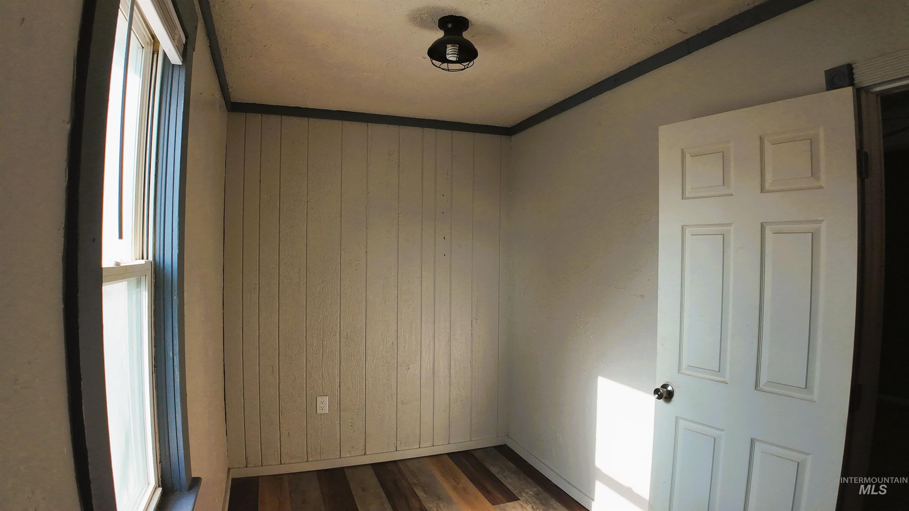 Unfurnished room featuring wood walls, ornamental molding, and dark wood-style flooring