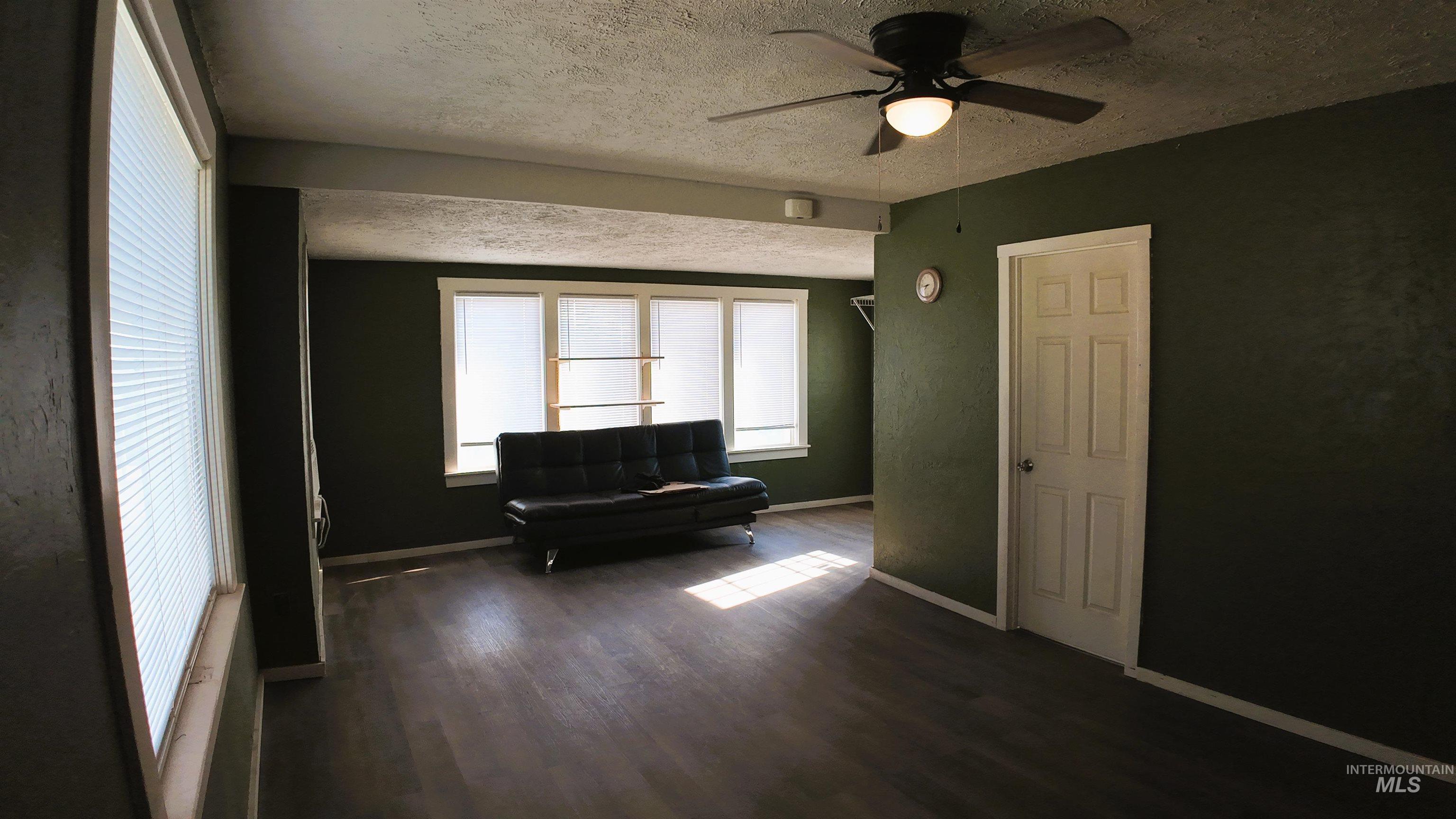 Living area with a textured ceiling, dark wood-type flooring, and ceiling fan