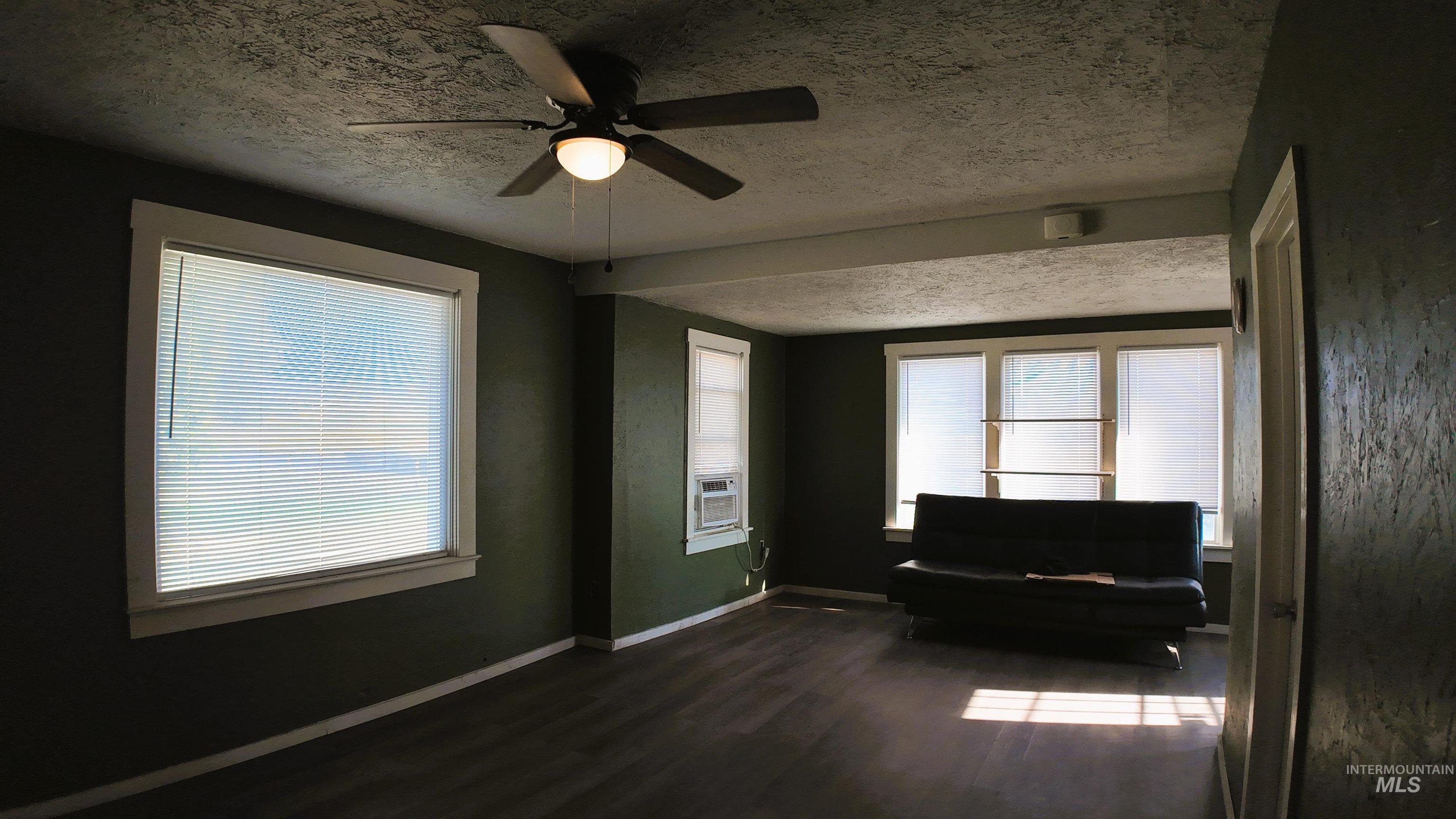 Living area with a textured ceiling, a ceiling fan, and dark wood-type flooring