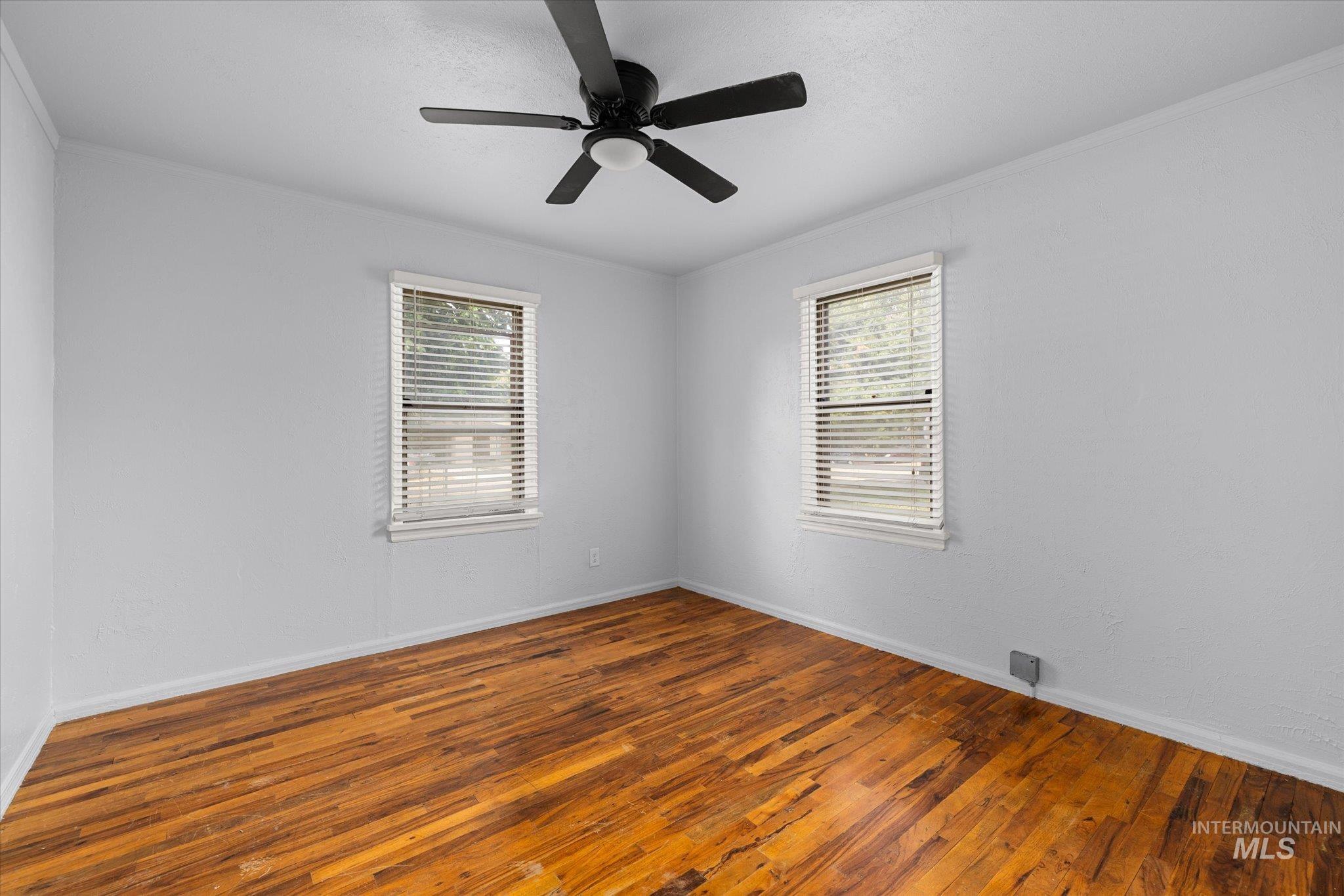 Empty room with dark wood-type flooring, crown molding, and a ceiling fan