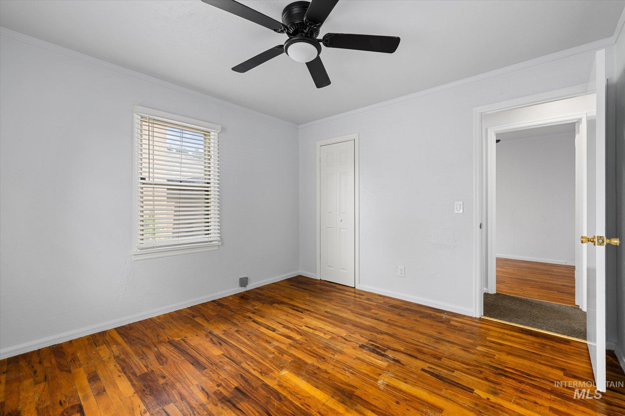 Unfurnished bedroom with crown molding, dark wood-type flooring, ceiling fan, and a closet