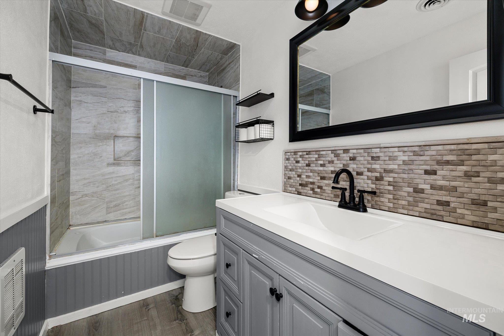 Full bath featuring bath / shower combo with glass door, dark wood-type flooring, vanity, and backsplash
