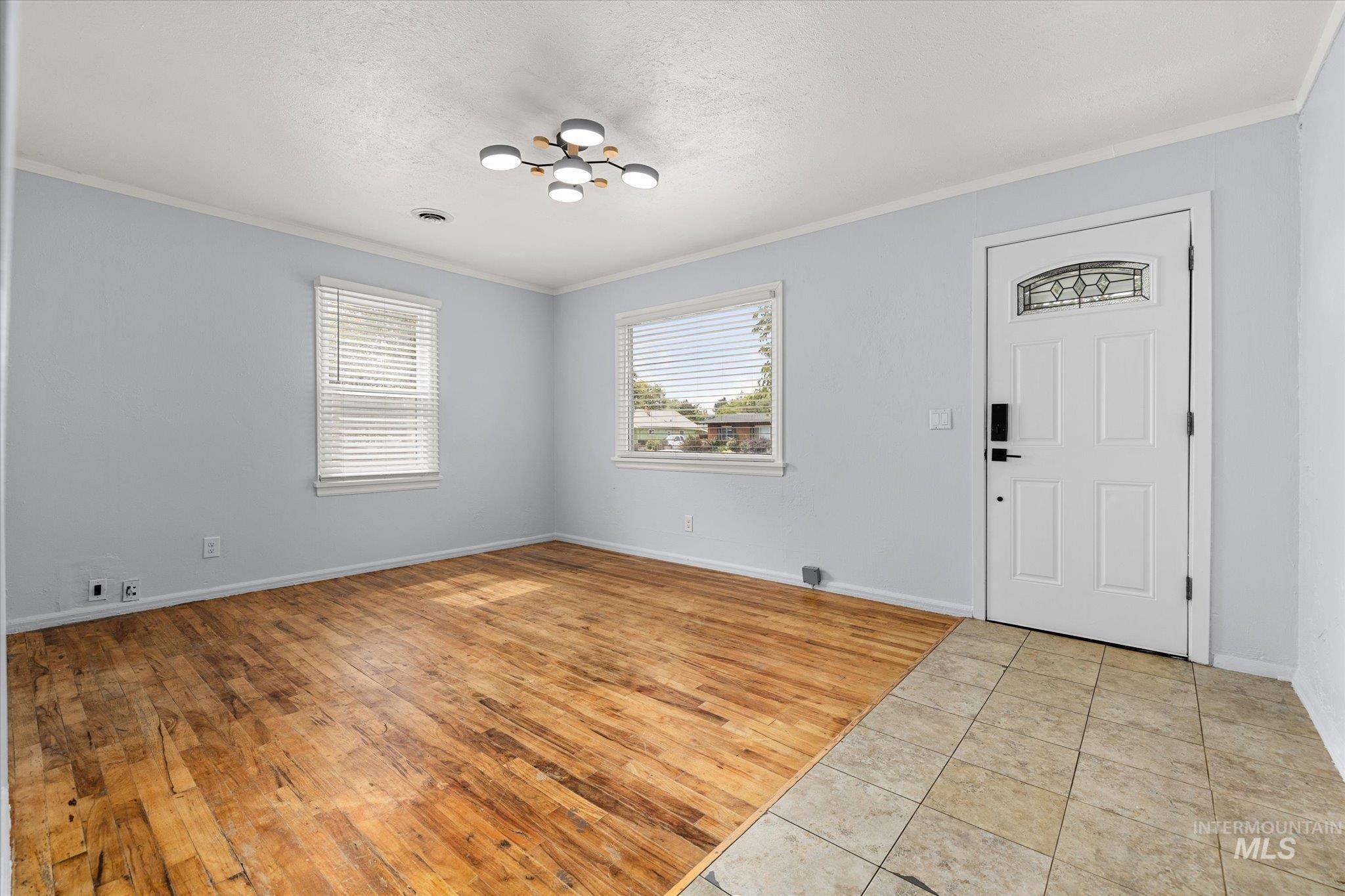 Entryway with crown molding, light wood-type flooring, a chandelier, and a textured ceiling