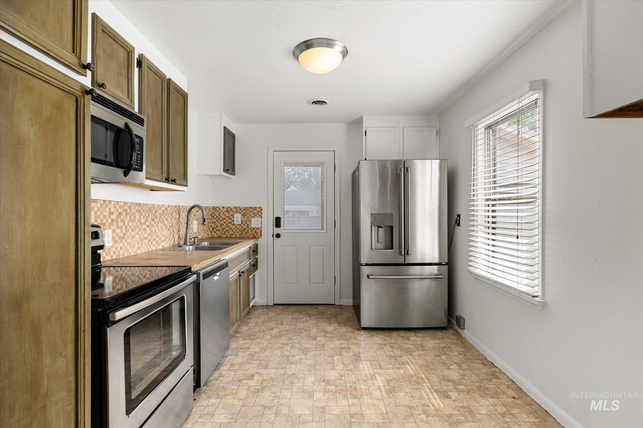 Kitchen with appliances with stainless steel finishes, backsplash, and light countertops