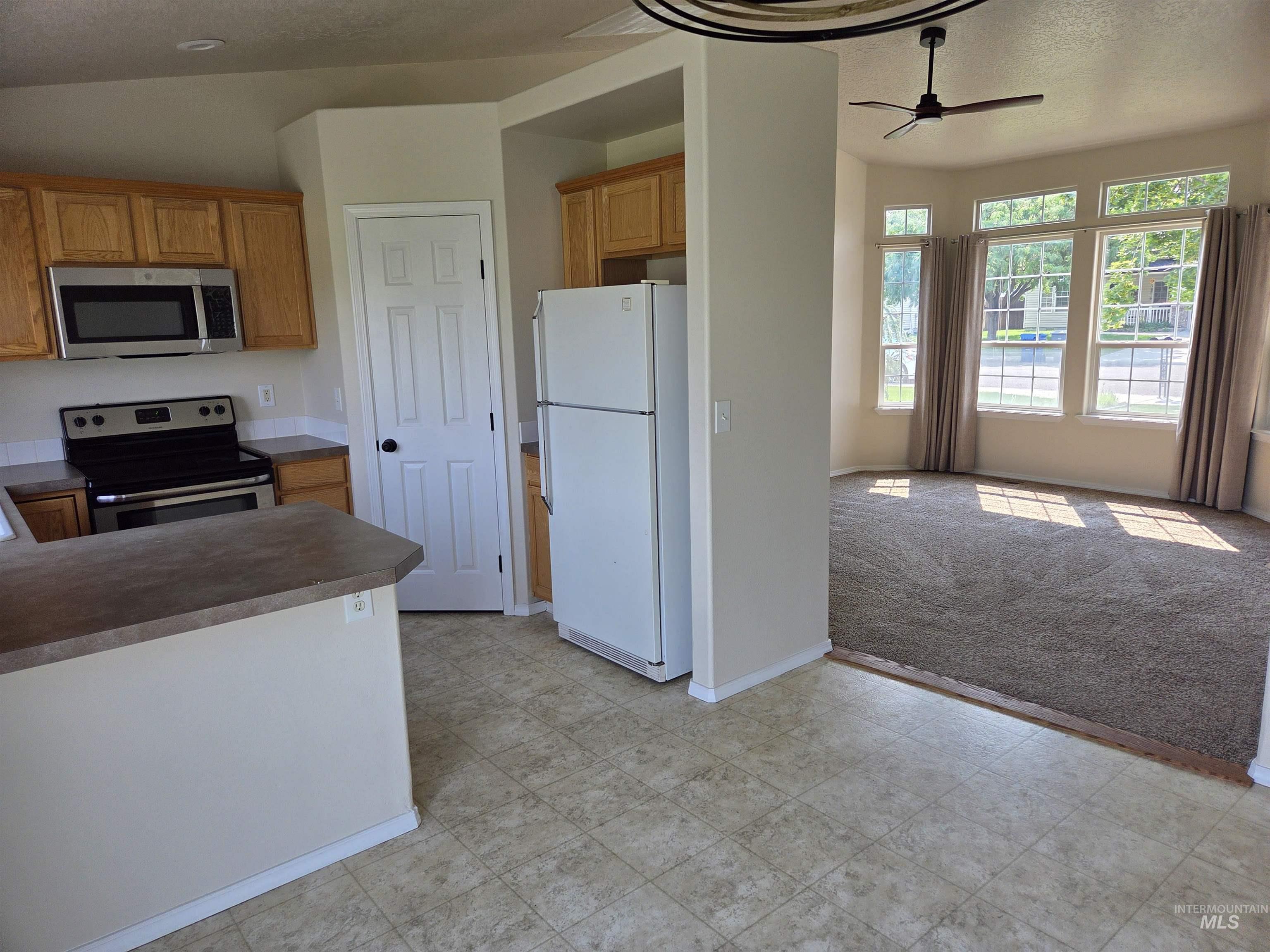 Kitchen with dark countertops, appliances with stainless steel finishes, a textured ceiling, ceiling fan, and light colored carpet