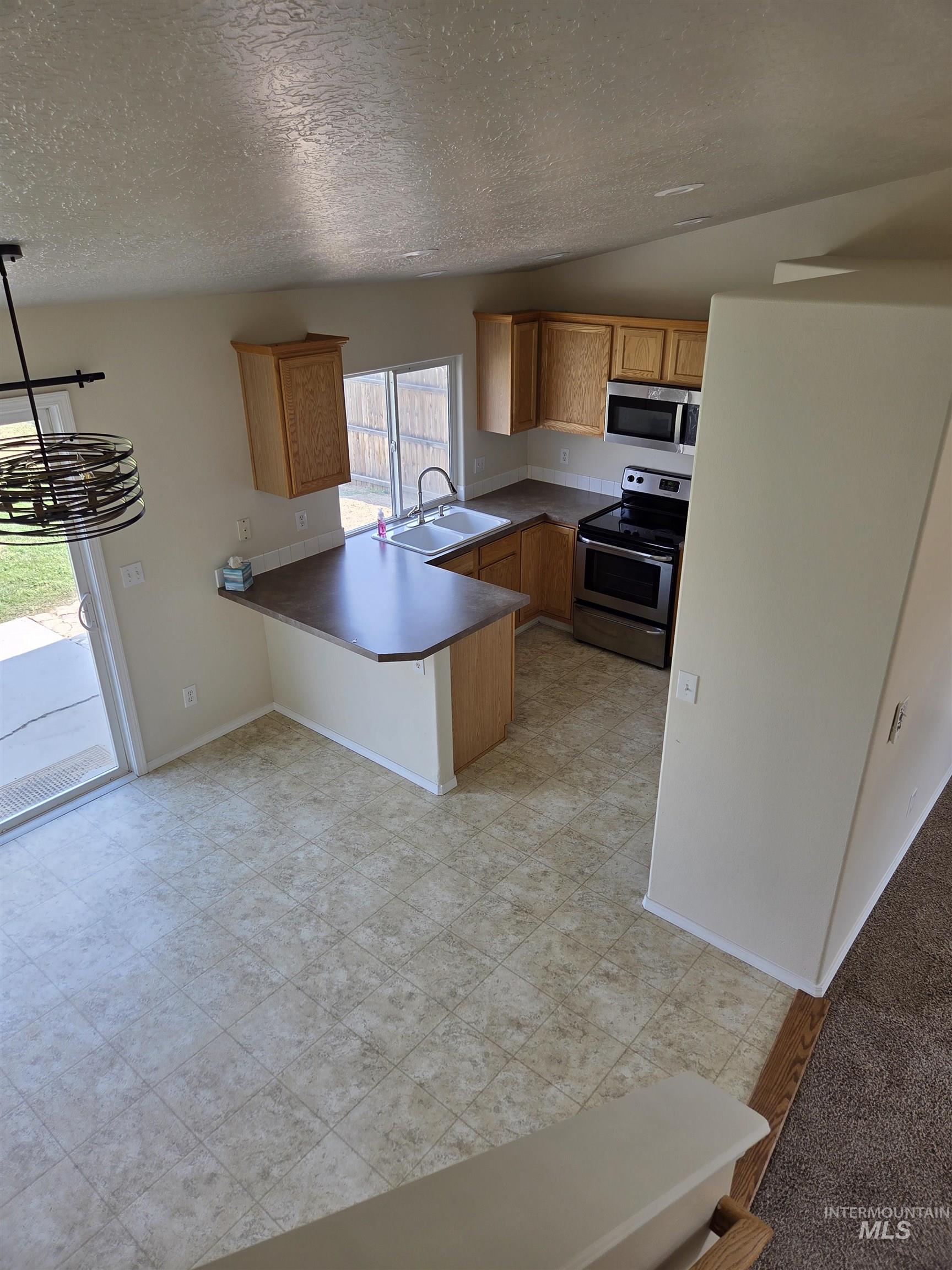 Kitchen featuring a peninsula, appliances with stainless steel finishes, a textured ceiling, dark countertops, and brown cabinetry