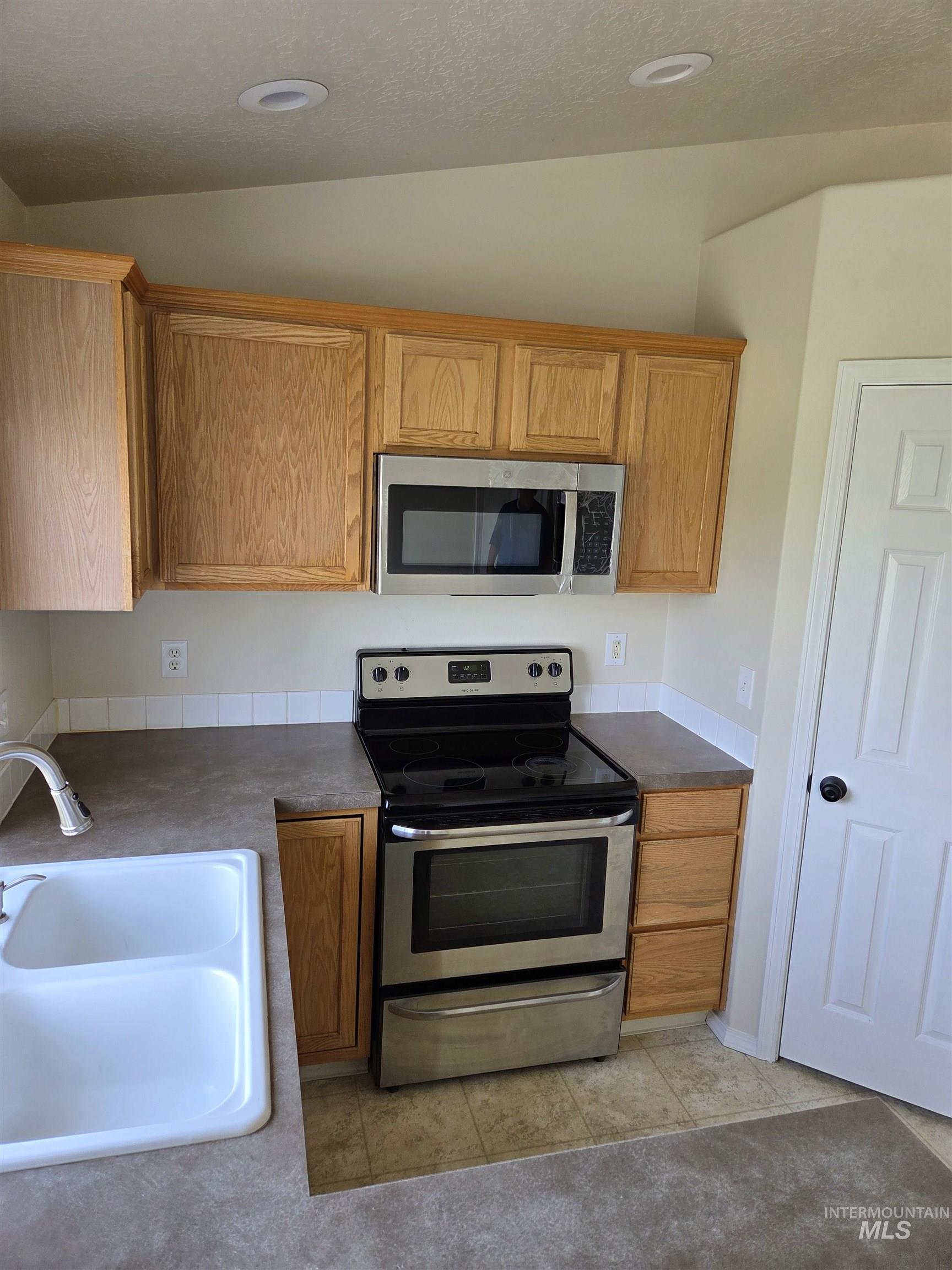 Kitchen with stainless steel appliances, dark countertops, light tile patterned floors, brown cabinets, and a textured ceiling