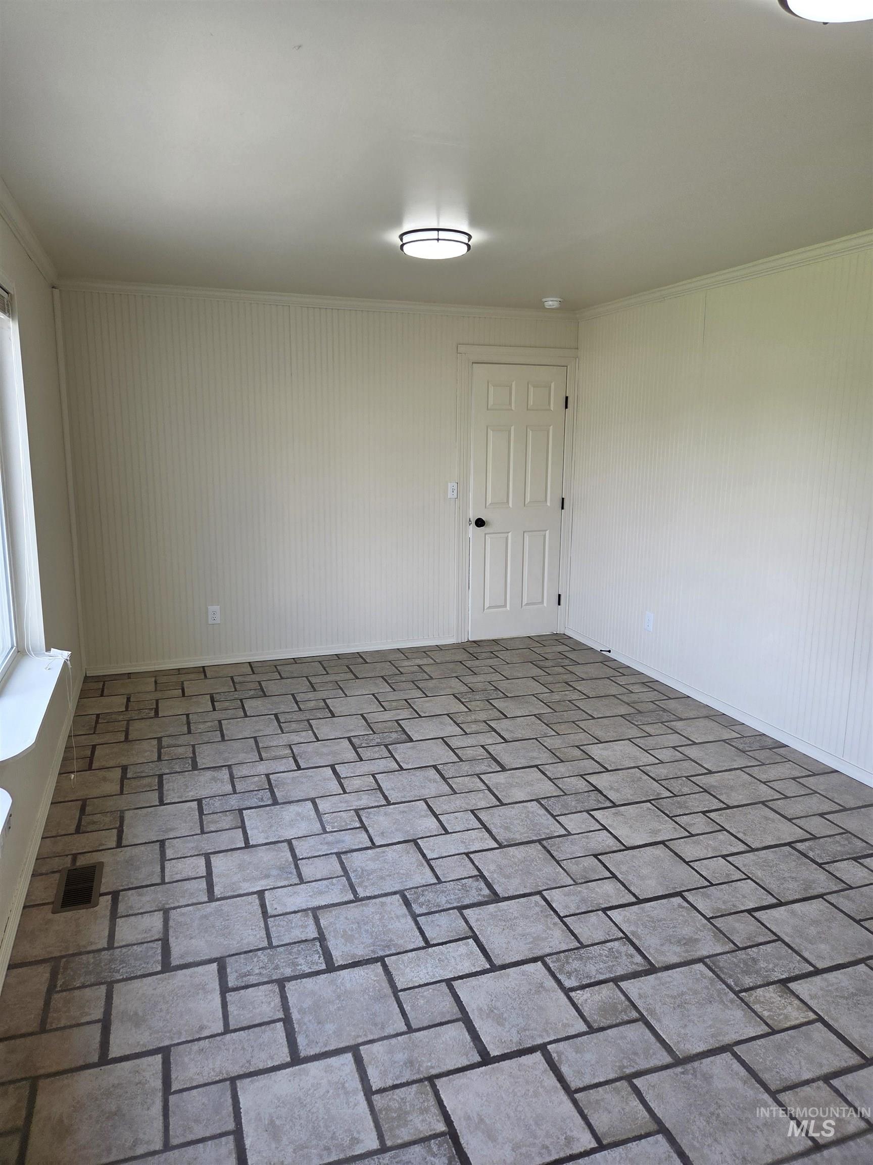 Empty room featuring brick patterned floors and crown molding