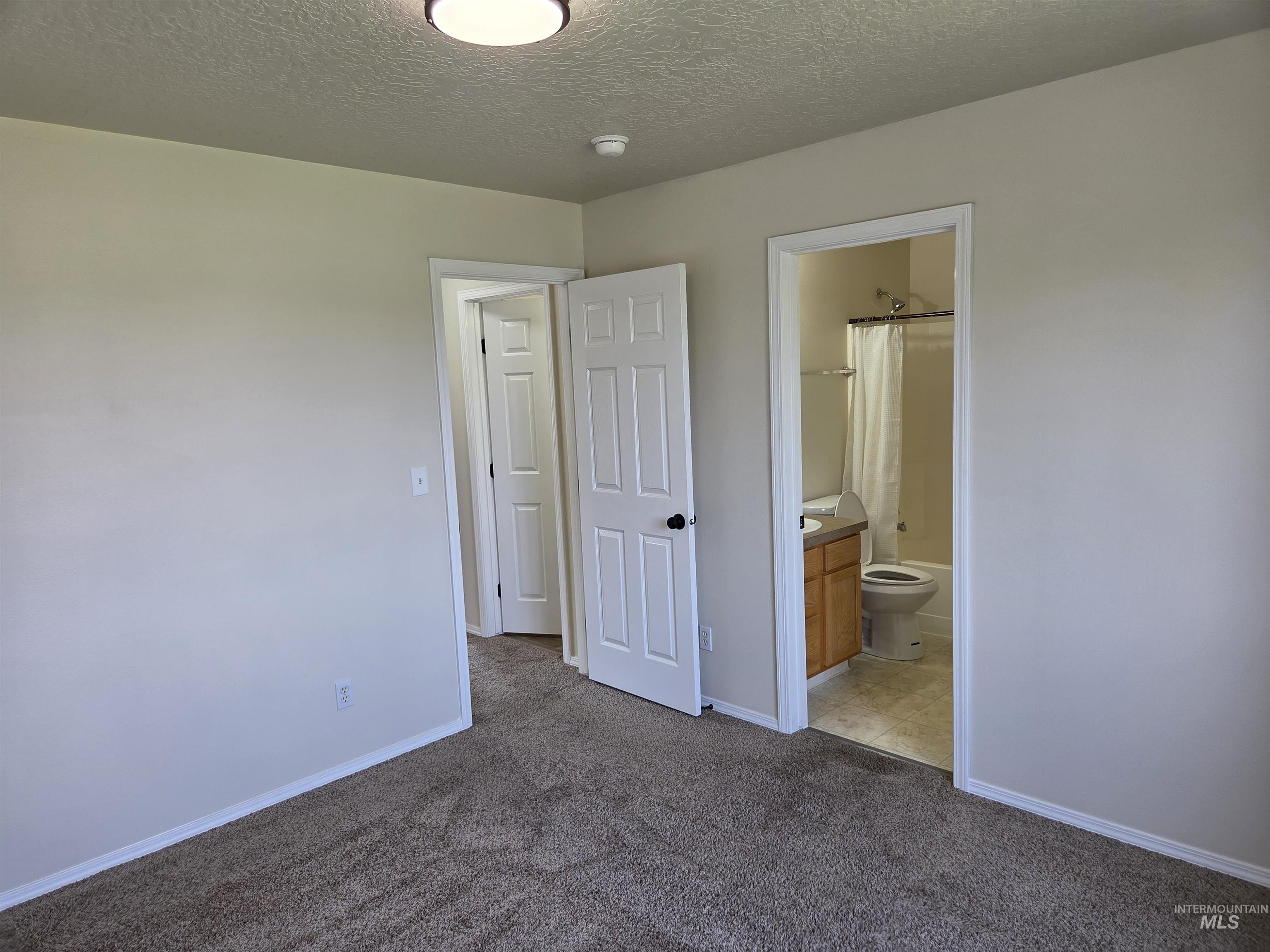 Unfurnished bedroom featuring dark carpet, a textured ceiling, and ensuite bathroom
