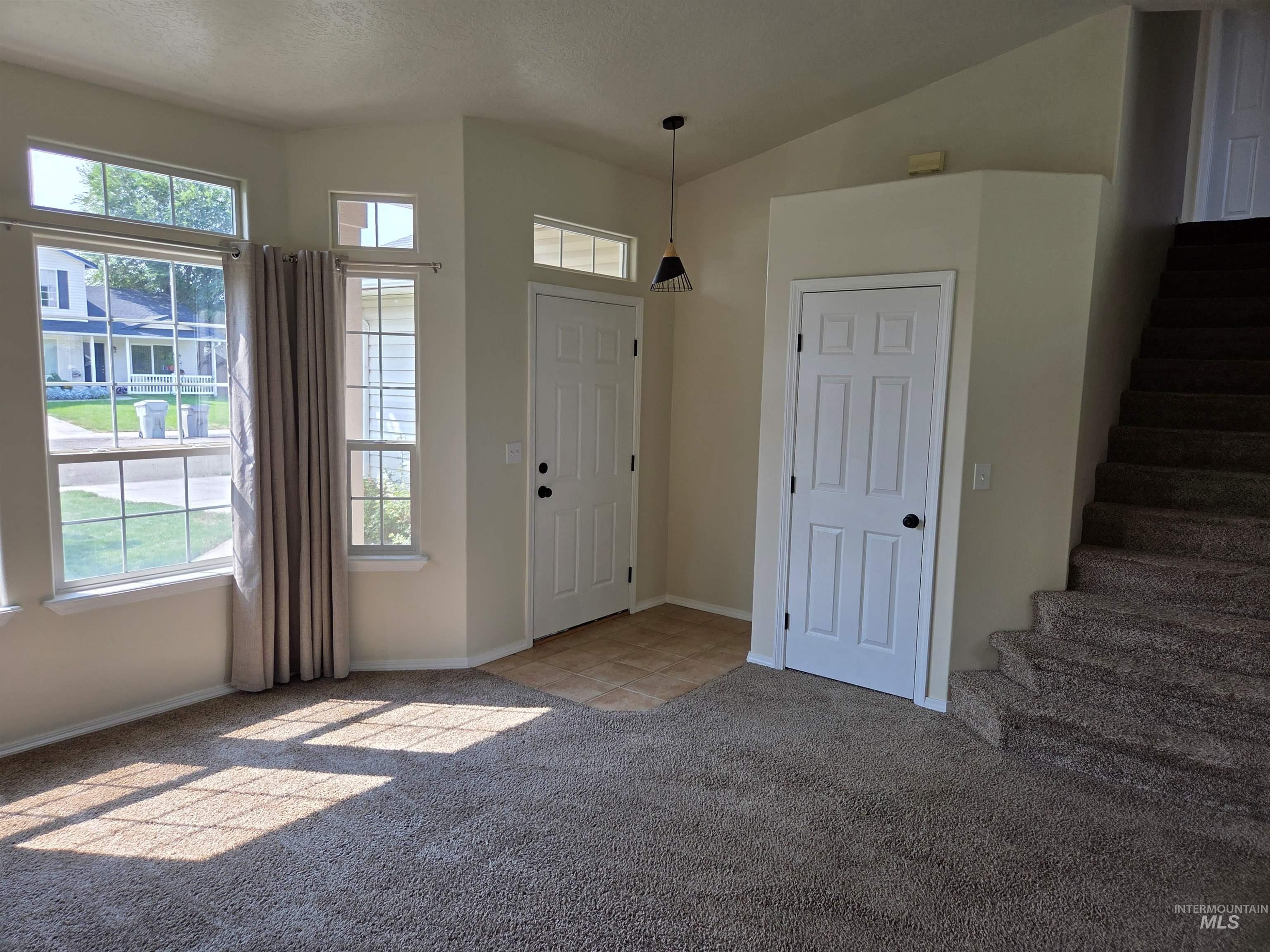 Foyer with light colored carpet, stairway, vaulted ceiling, and a textured ceiling